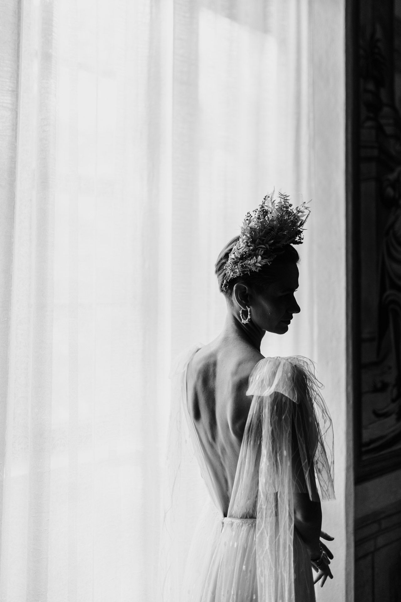 Artistic black and white portrait of figure in wedding attire against bright window.