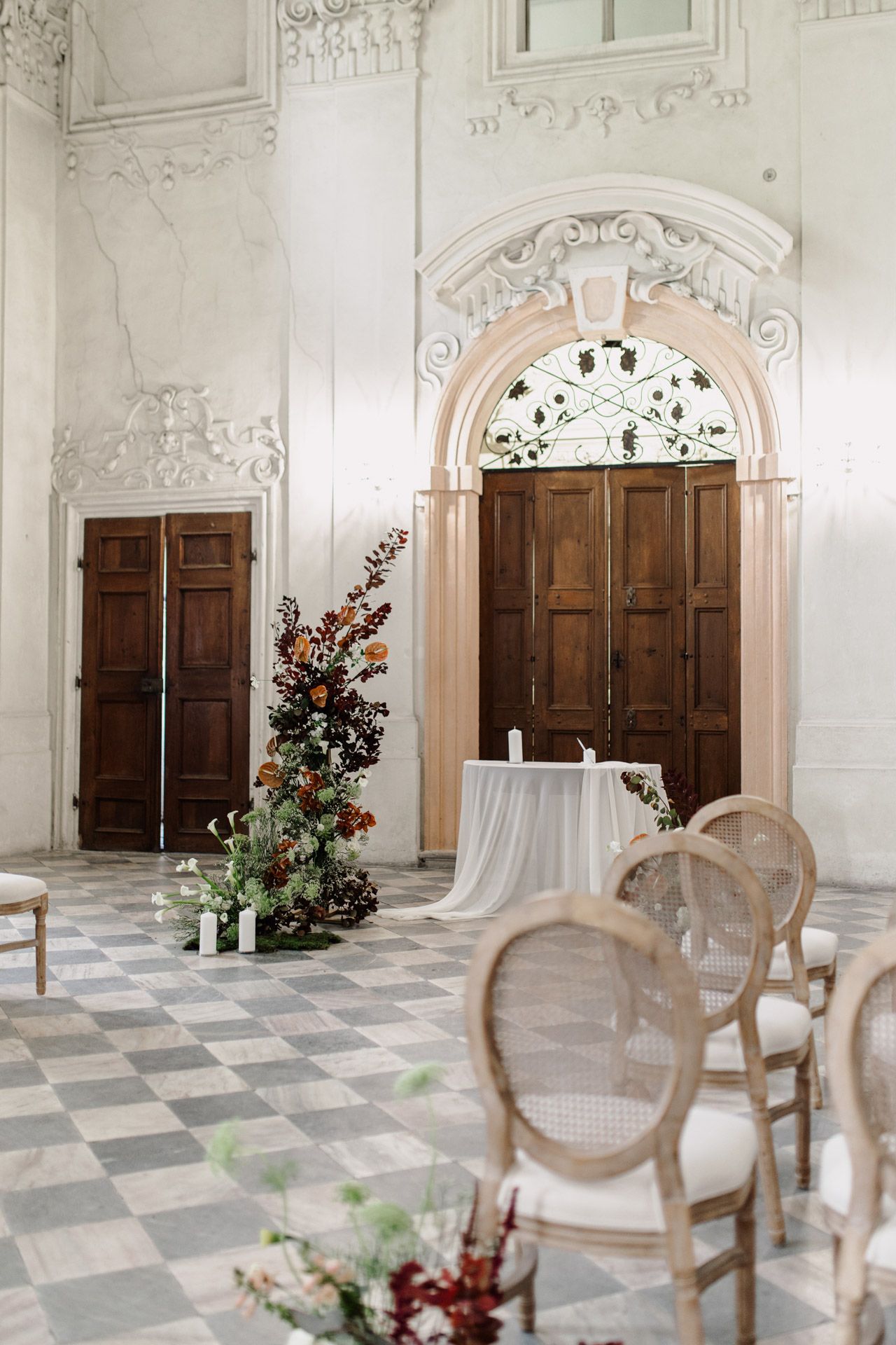 Classic white room with wooden doors, ornate moldings, and vintage chairs arranged for a ceremony.