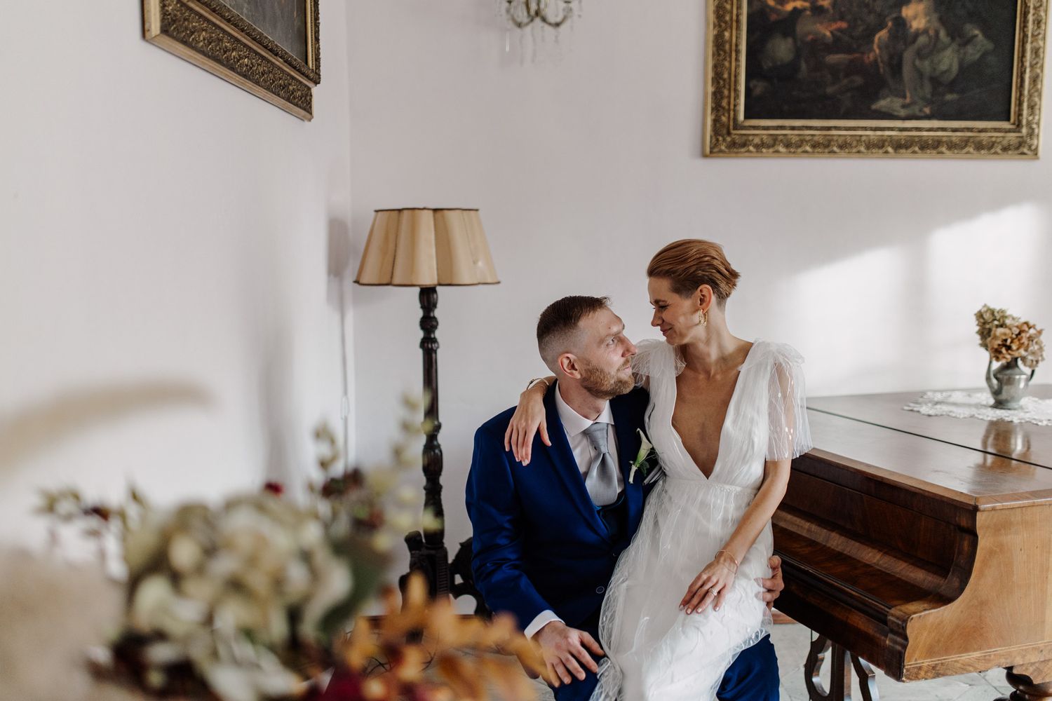 Intimate wedding photo of couple by piano in elegantly decorated room with artwork.