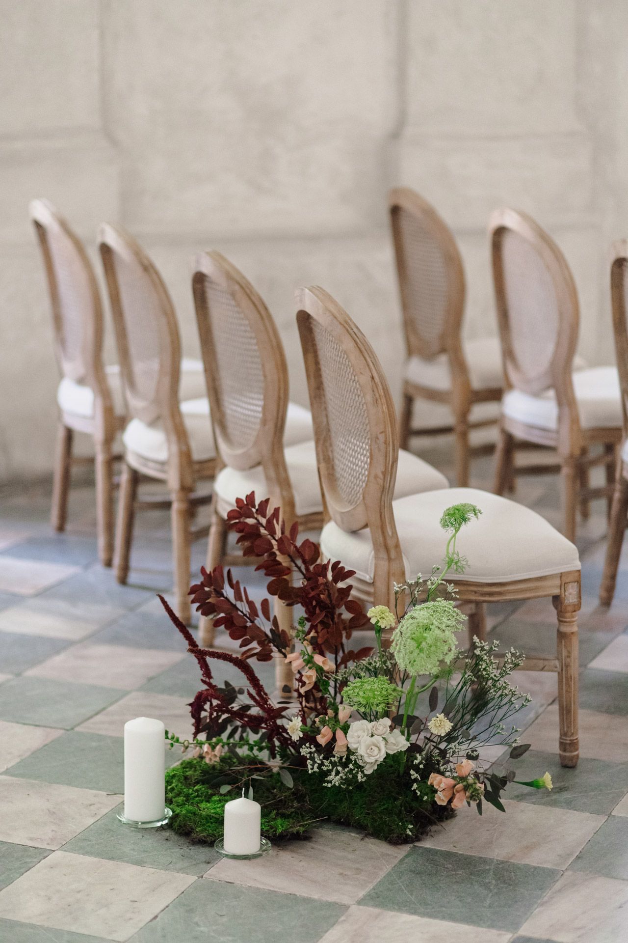 Floral arrangement with burgundy leaves and candles decorating elegant cane chairs at a wedding venue.