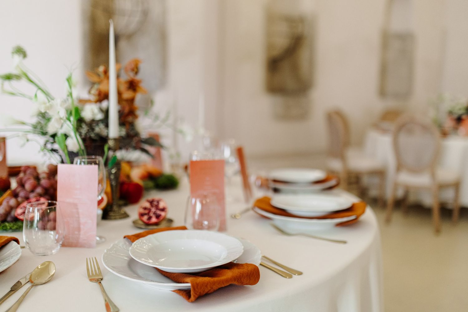 Wedding table setup with white plates, terracotta chargers, and pink glassware against white linens.