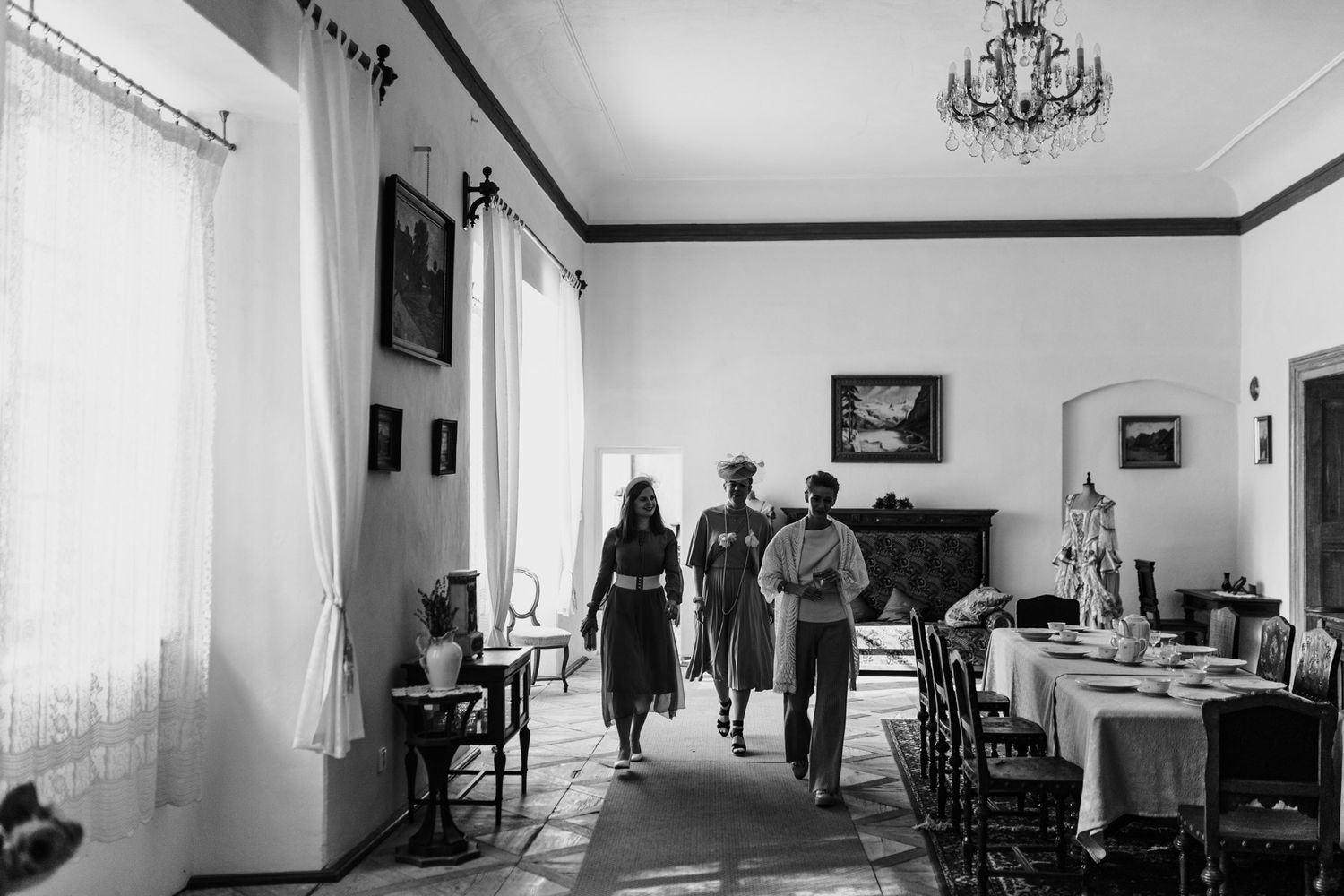 Black and white photograph of an elegant dining room with people walking through.