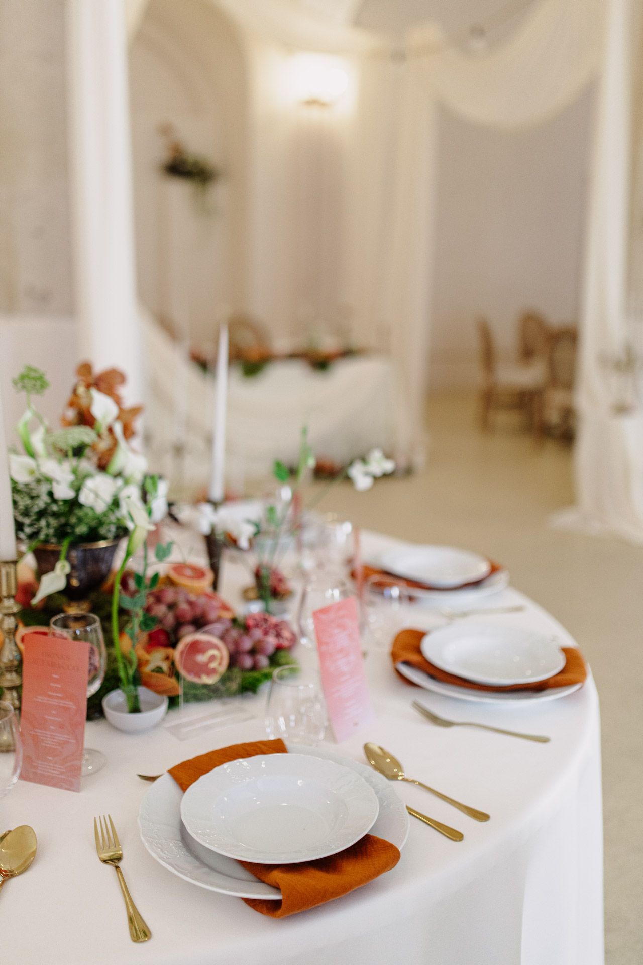 Elegant table setting with white plates, copper chargers, and pink floral centerpieces in a bright white room.