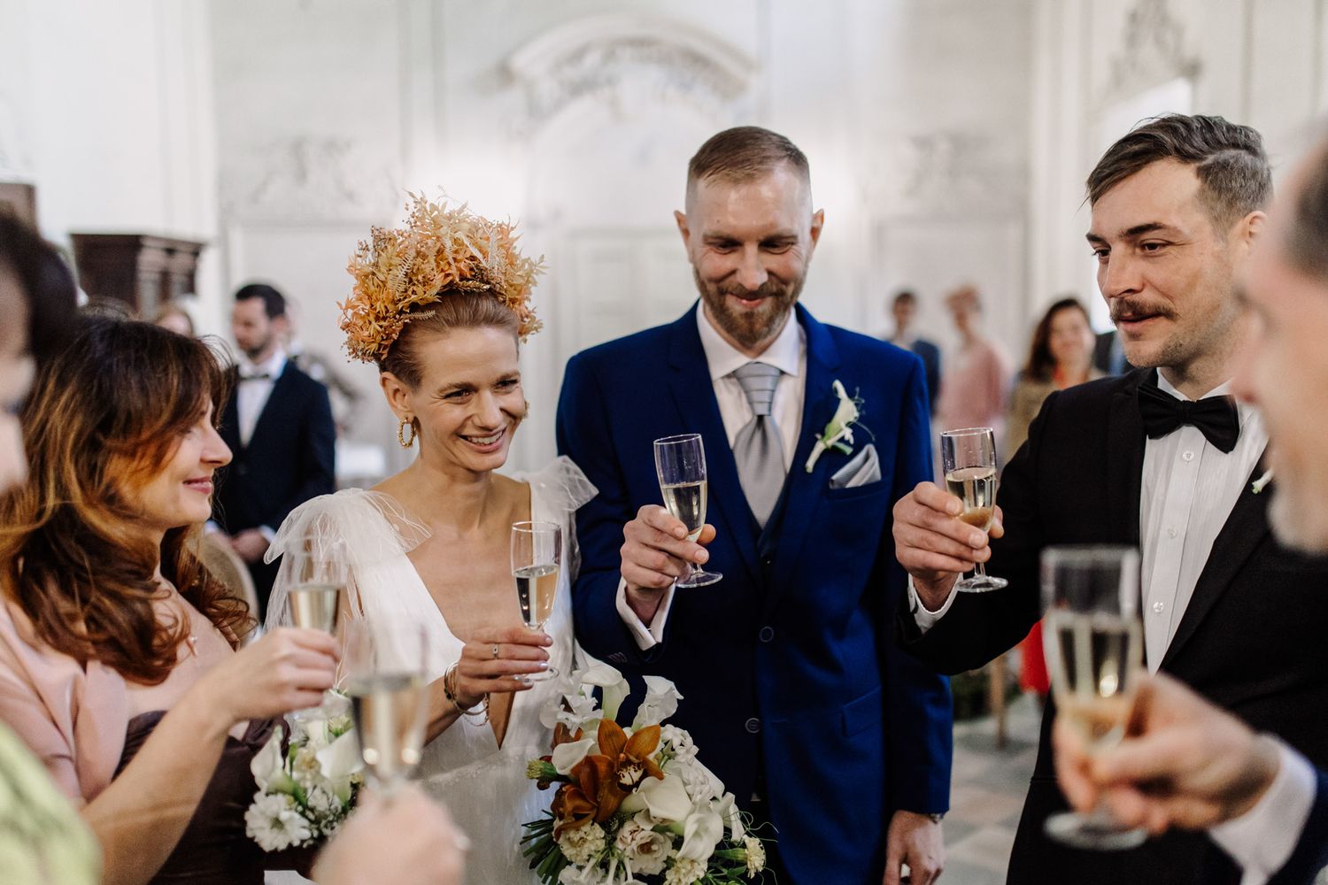 Wedding party toasting with champagne in elegant white hall.