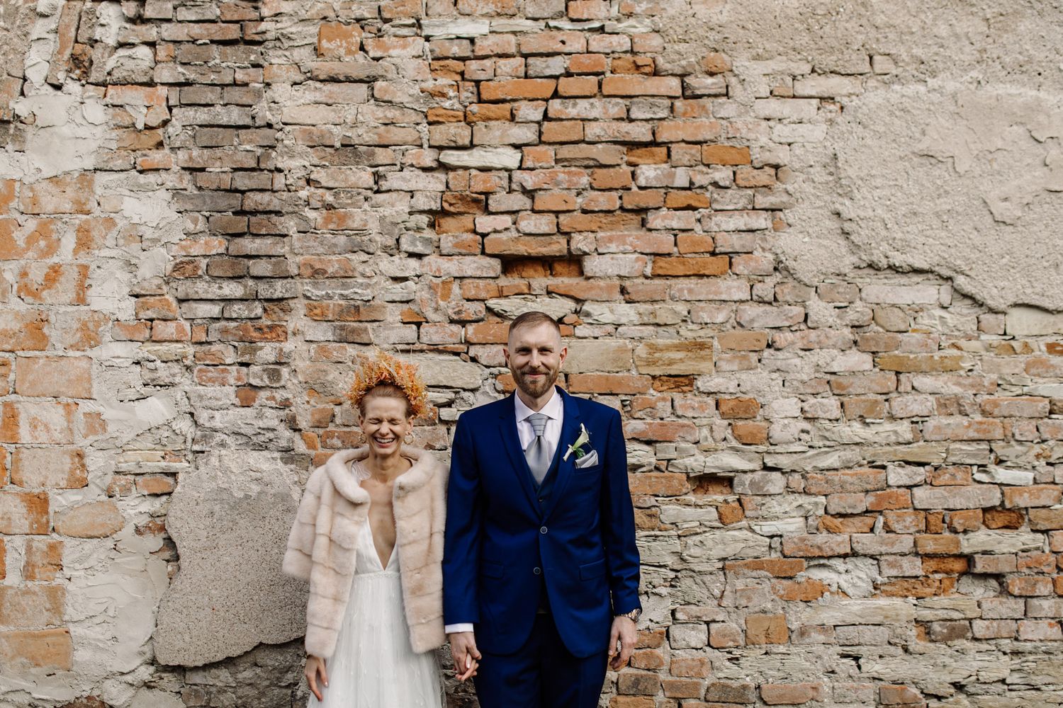 Wedding couple poses against rustic brick wall with weathered texture and charm.