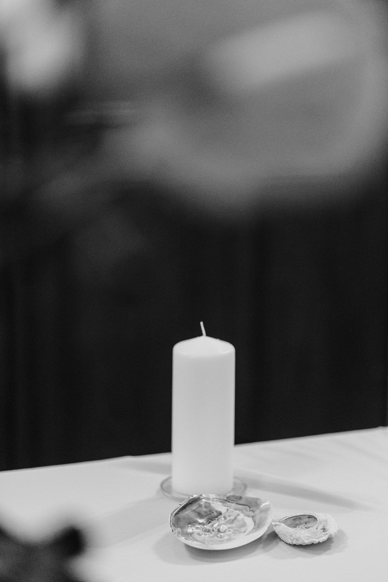 White pillar candle on crystal holders against dark background in artistic black and white.