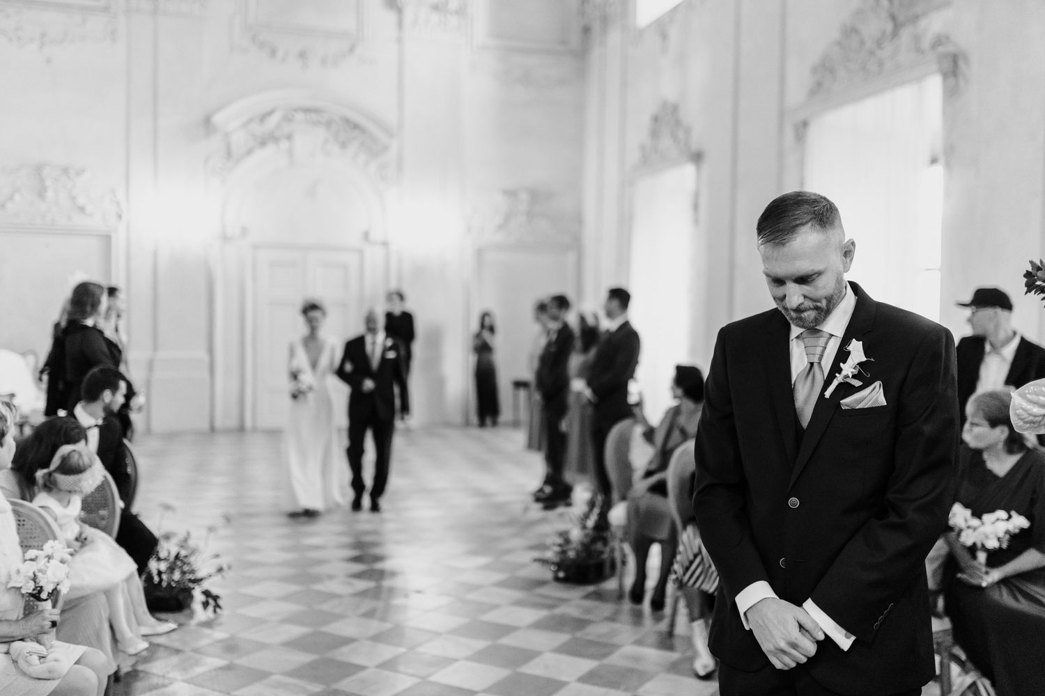 Black and white photo of wedding ceremony in grand white baroque hall.