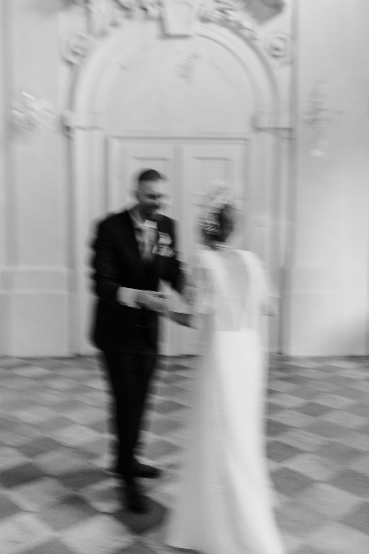 Artistic blurred black and white photo of newlyweds standing before decorative white archway.