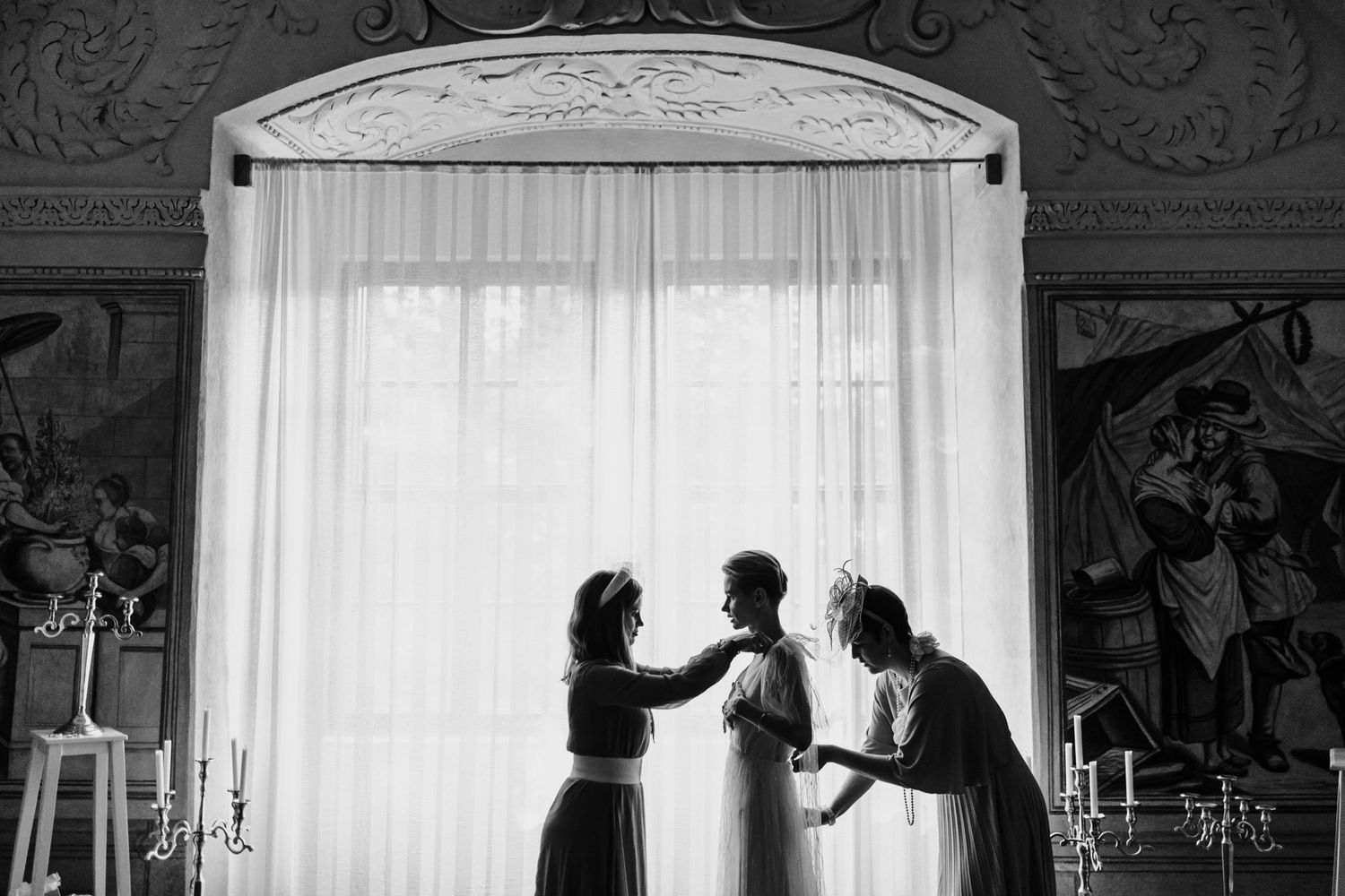 Black and white silhouette of figures against window during wedding preparations.