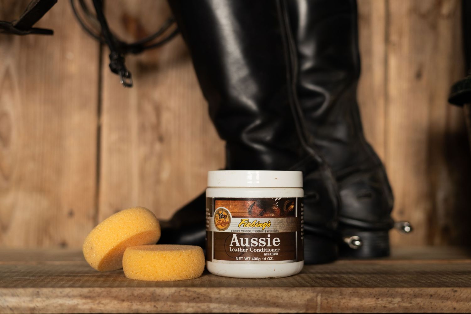 Leather riding boots and yellow sponges next to an Aussie leather care product container.