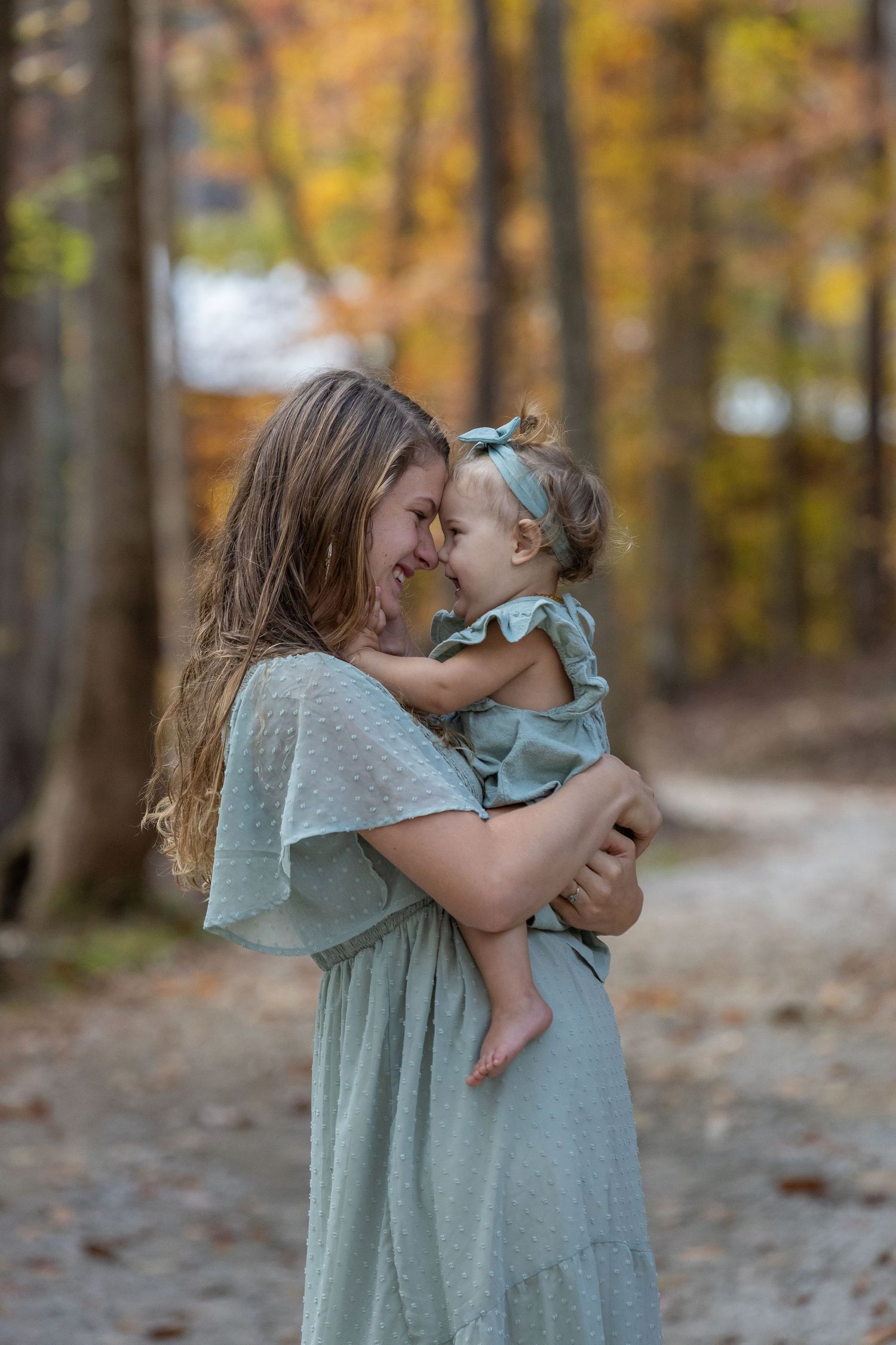 A tender moment shared between a parent and child wearing matching sage green dresses in an autumn forest setting.