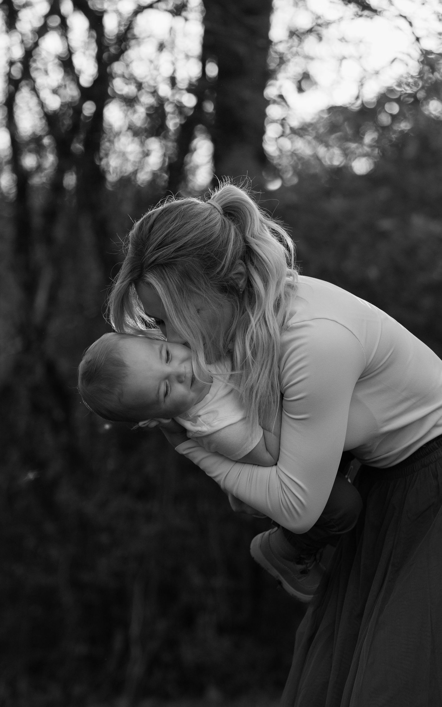 A tender moment between parent and baby captured in black and white against a forest backdrop.