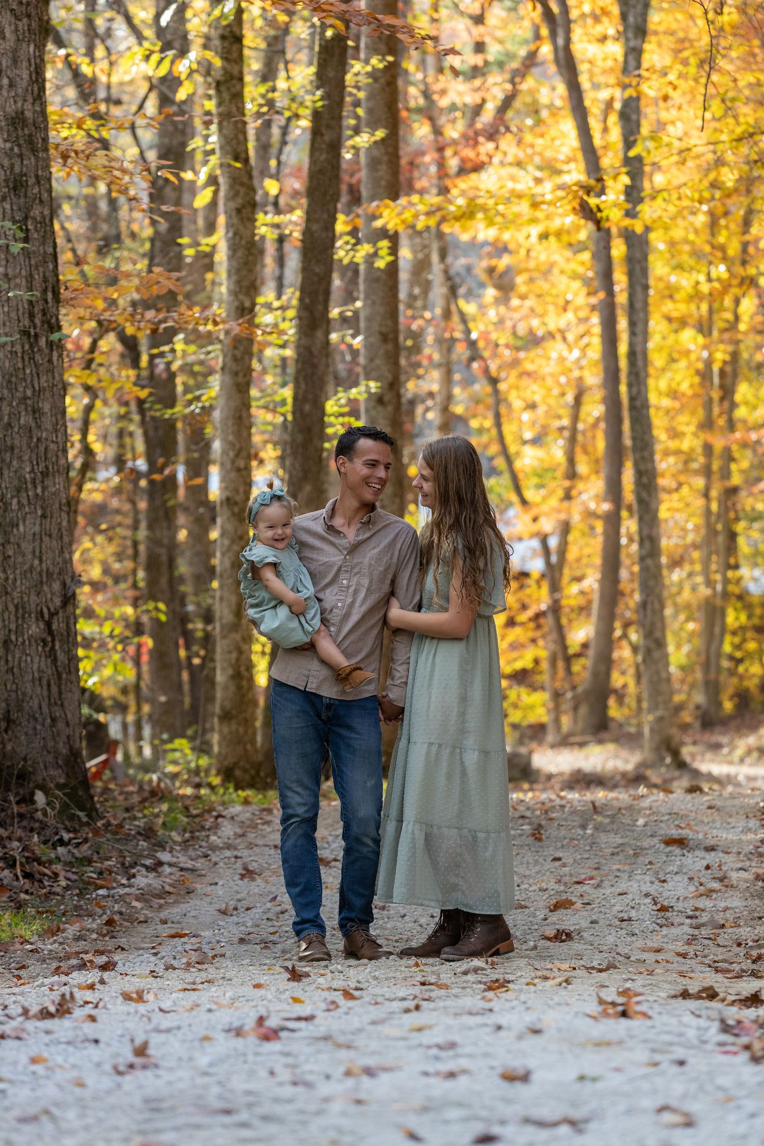 A couple walks along a forest path surrounded by vibrant fall foliage on an autumn day.