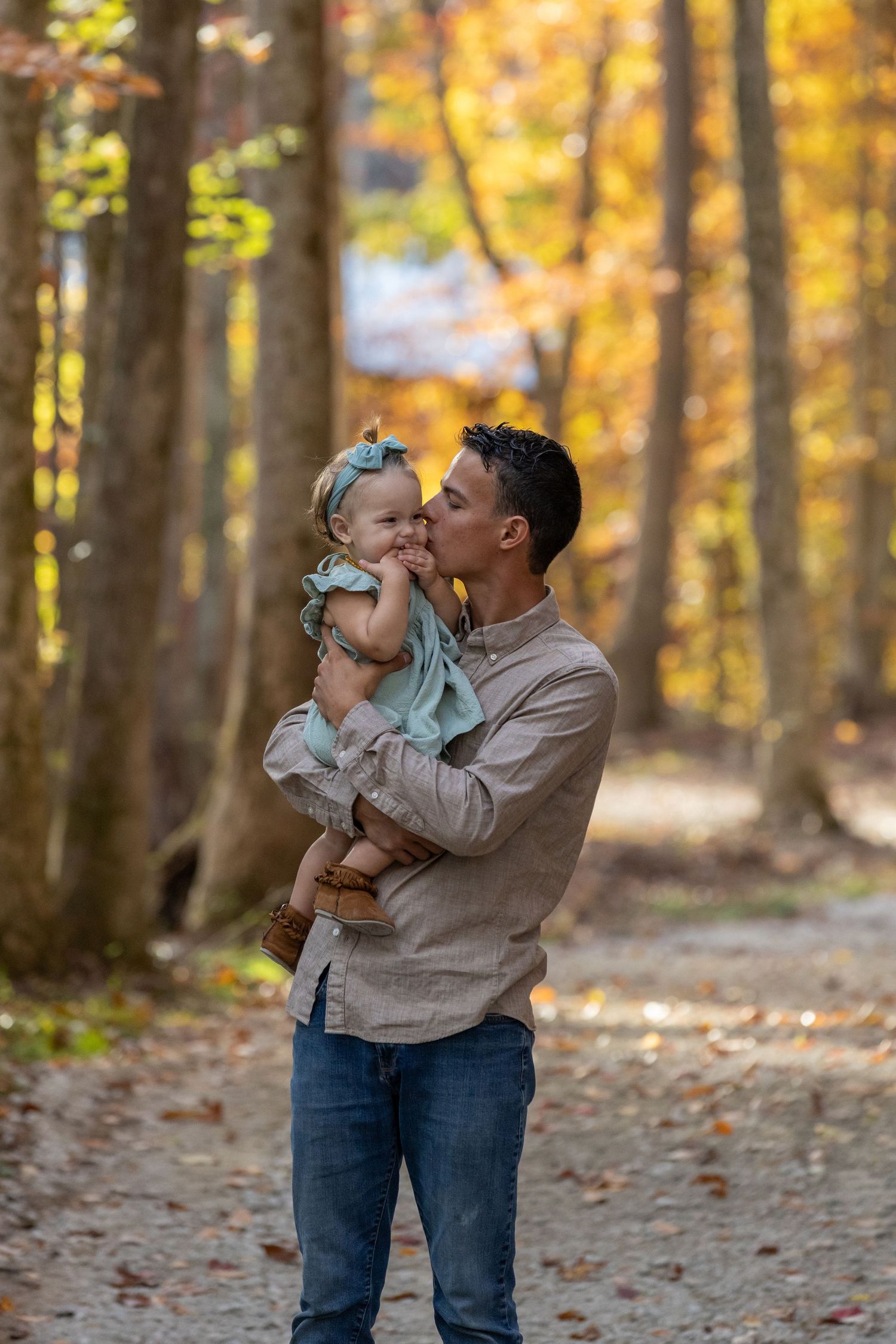 A sweet tender moment between a loving adult and baby surrounded by golden autumn foliage on a forest path.