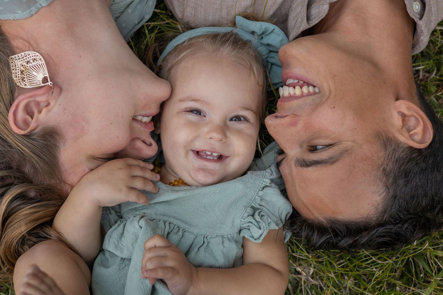 Family laying on grass together in a circle formation wearing light blue while laughing joyfully.