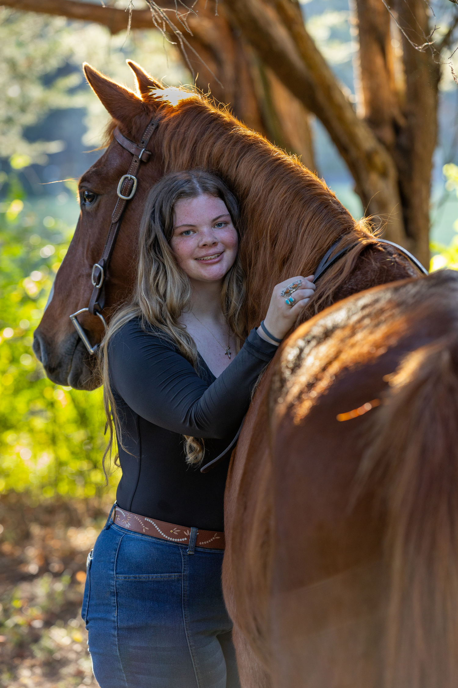 Horse and rider share a tender moment in sunlit wooded setting with warm golden lighting.