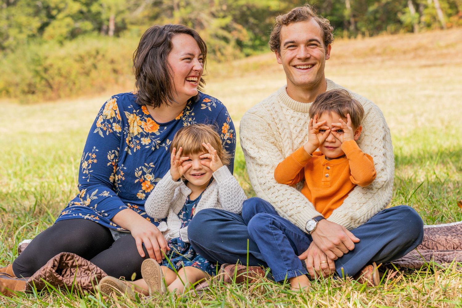 A playful family portrait with everyone laughing while sitting in a sunny autumn field.