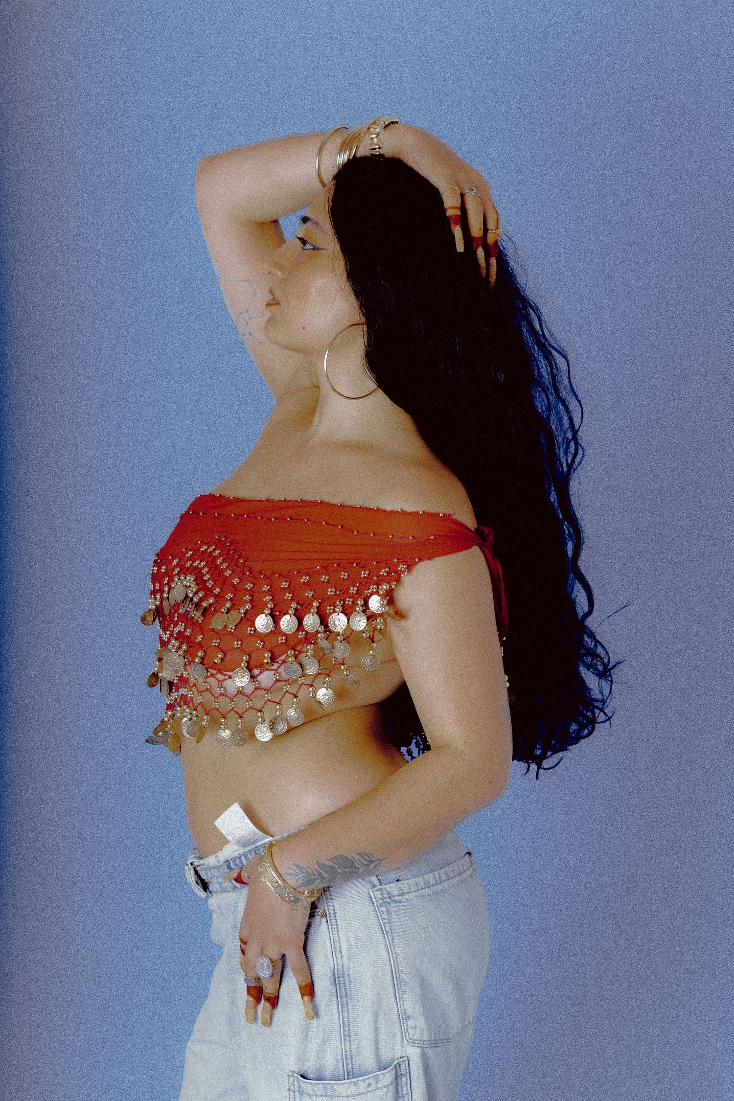 Portrait of Idiz, a multicultural Canadian musician with Arabic roots, wearing Belly Dancing Coin Belt standing in front of a blue backdrop