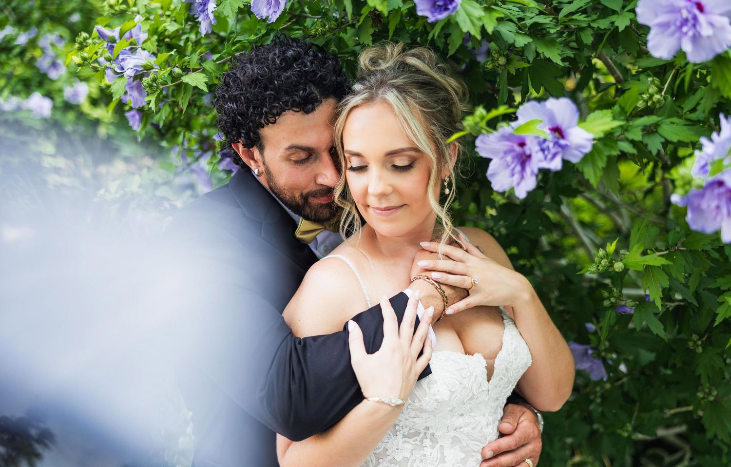 A romantic outdoor portrait of a couple embracing among blooming purple wisteria flowers.