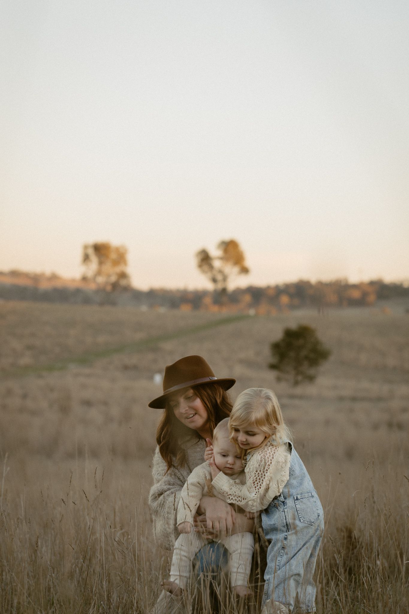 A mother and daughter share a tender moment together in a grassy field at sunset.