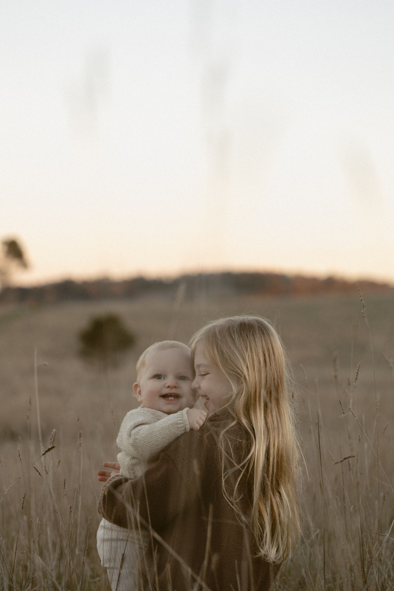A mother and baby share tender moments together at sunset in a golden wheat field.