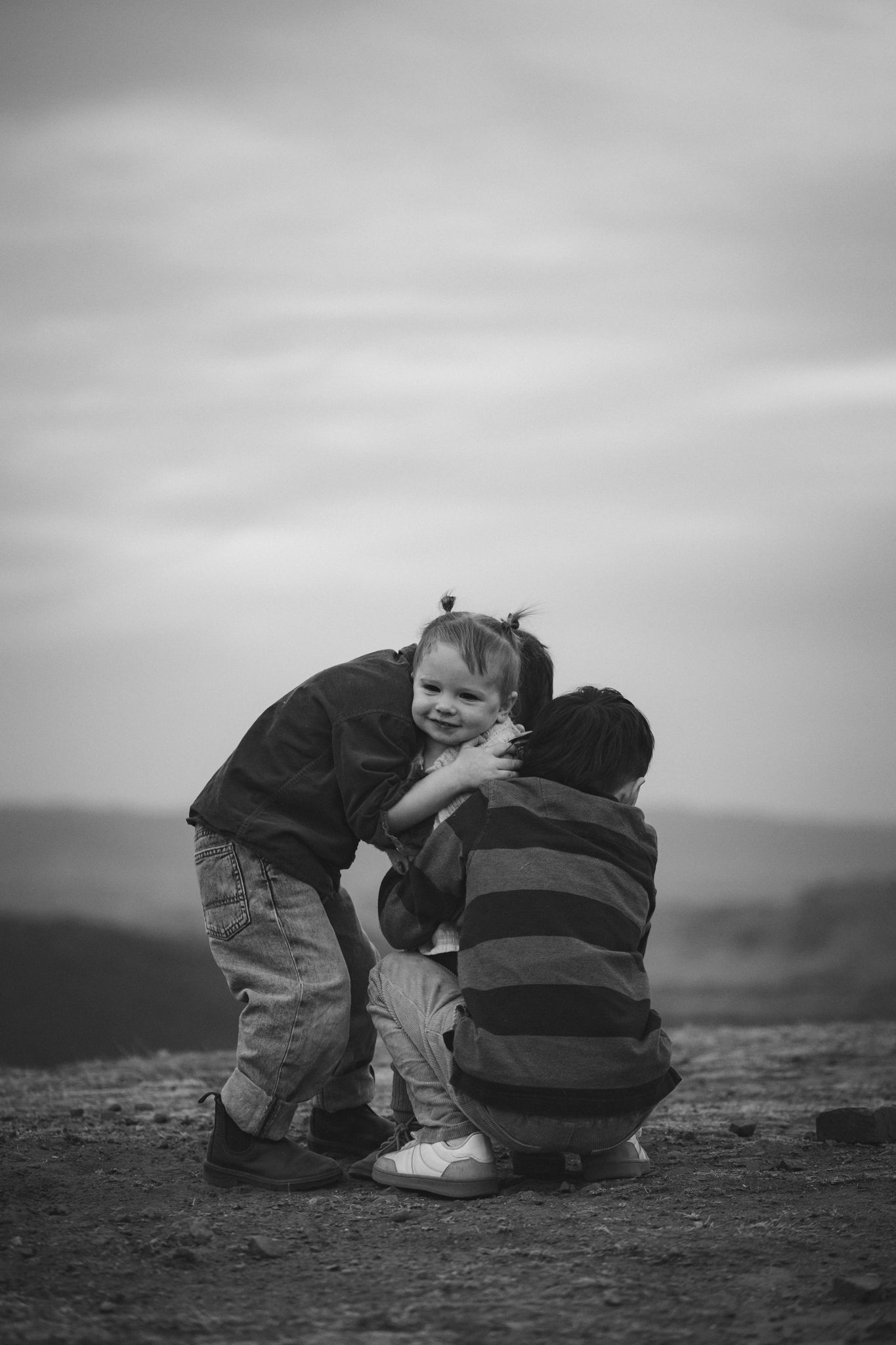 A heartwarming black and white photo of two children sharing an intimate moment on a hilltop with a blurred landscape behind.