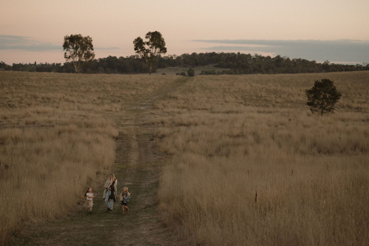 Two people walking along a dirt path through golden grassland at sunset with silhouetted trees on the horizon.