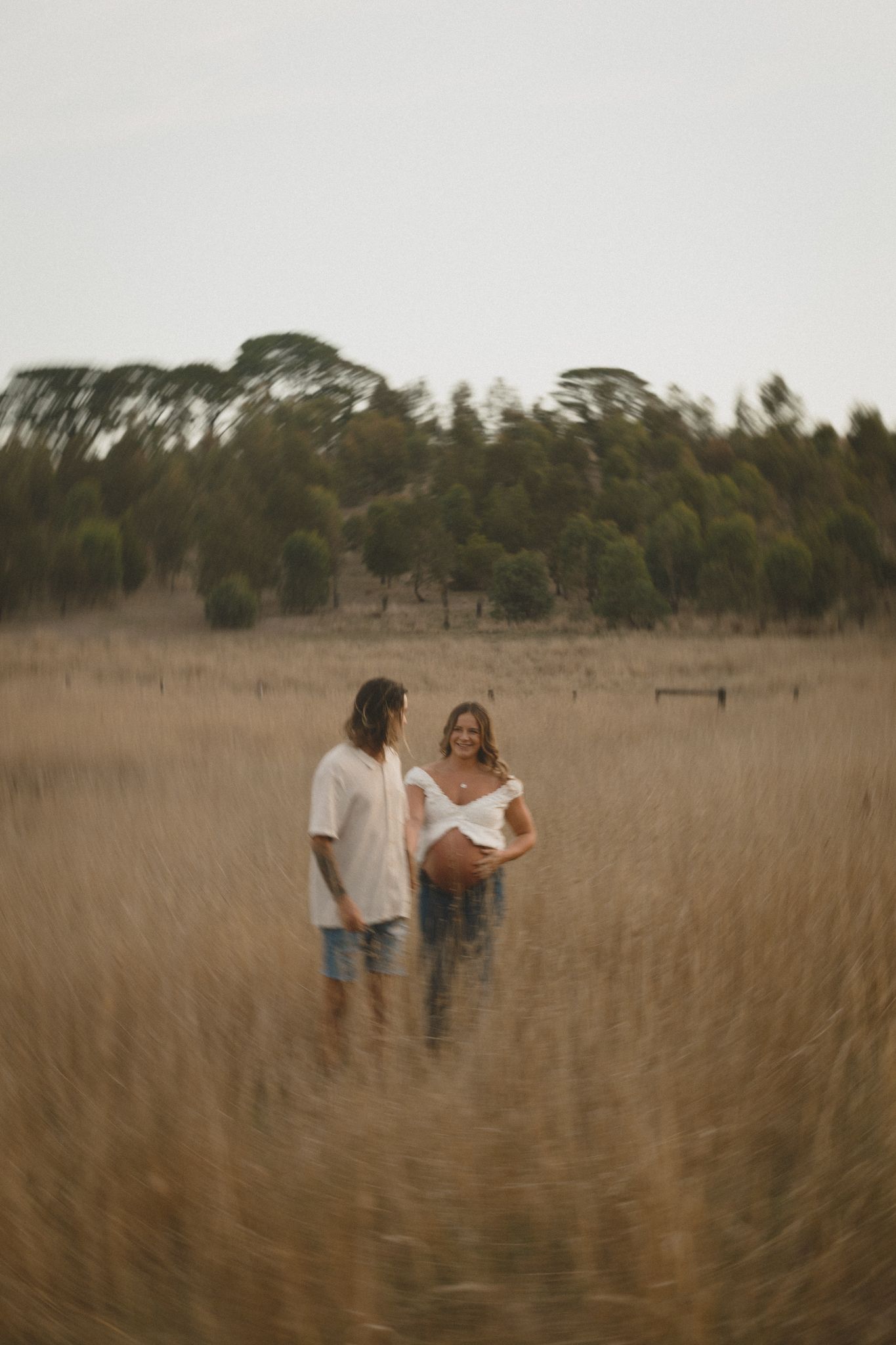 A couple walks together through a peaceful tall grass field on an overcast autumn day.