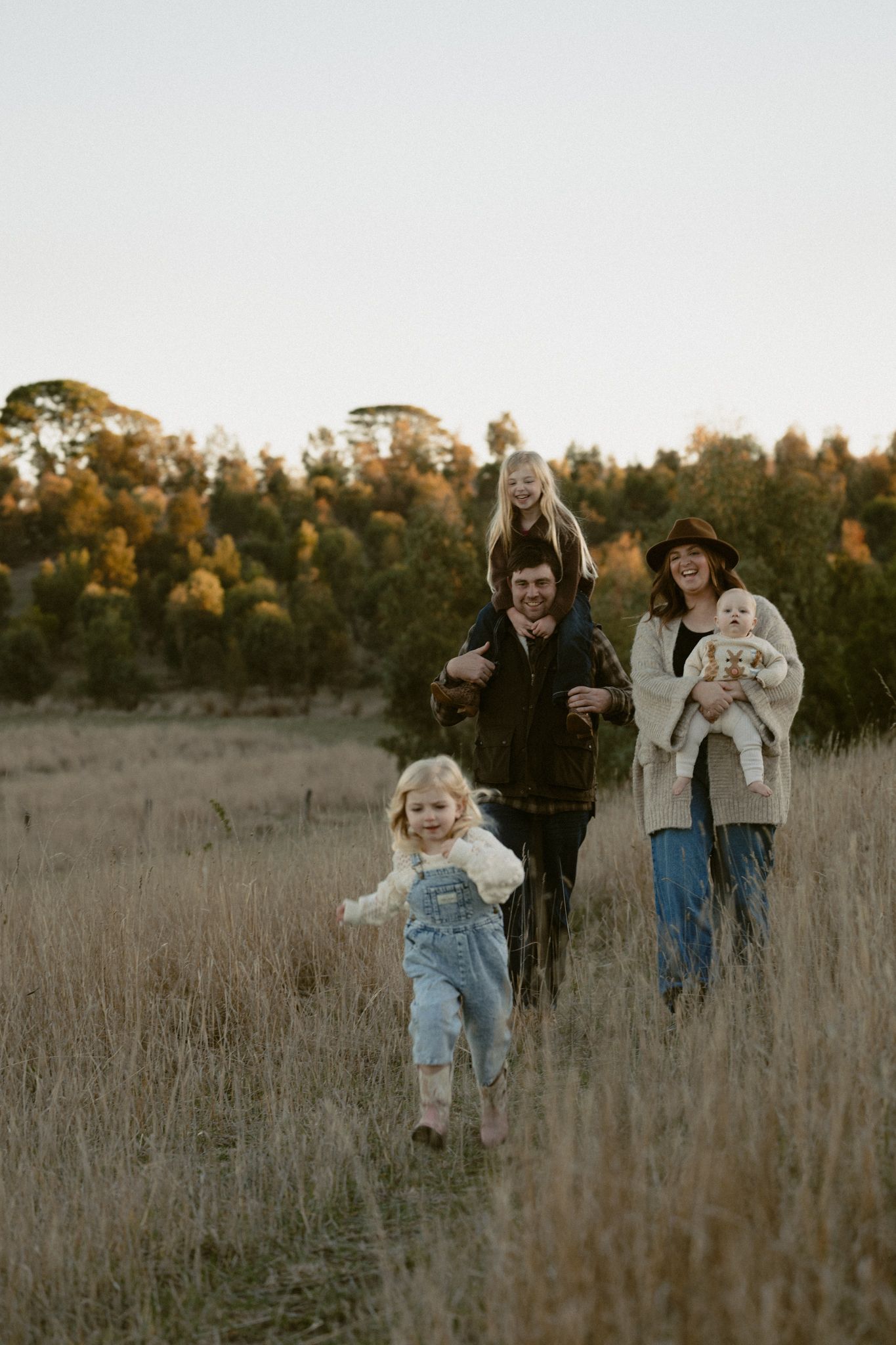 A happy family playing and running together in a golden autumn field at sunset.