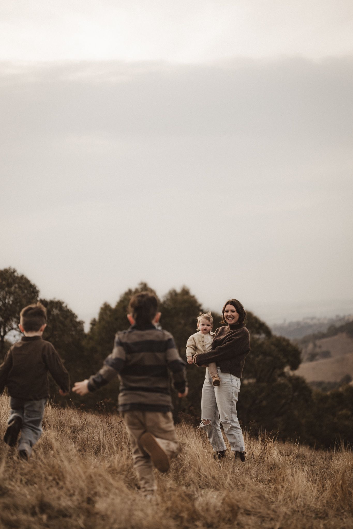 Children playing on a hillside at sunset with rolling hills and trees visible in the background.