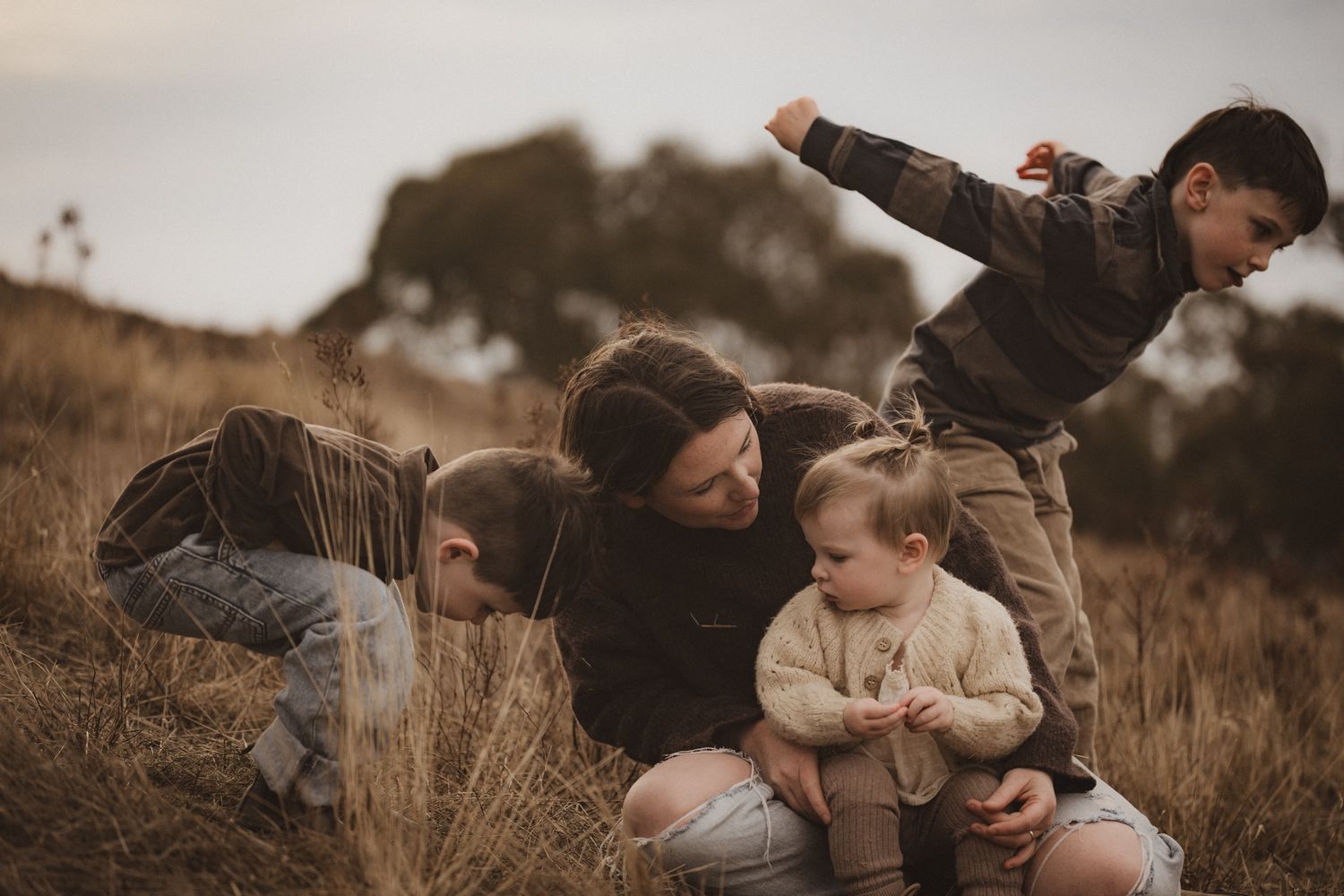 A family shares a playful moment together in a field of tall grass during golden hour.