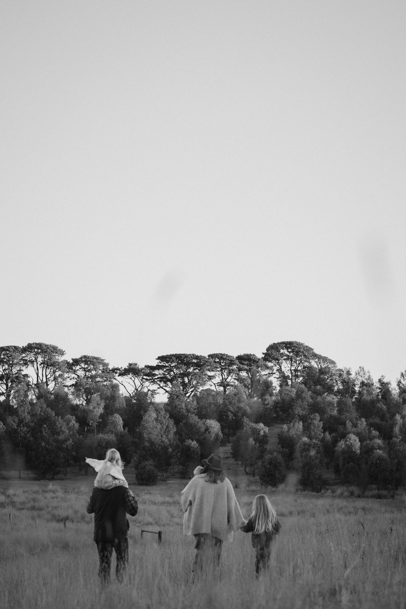 A black and white photograph of people walking through a field towards a treeline at dusk.