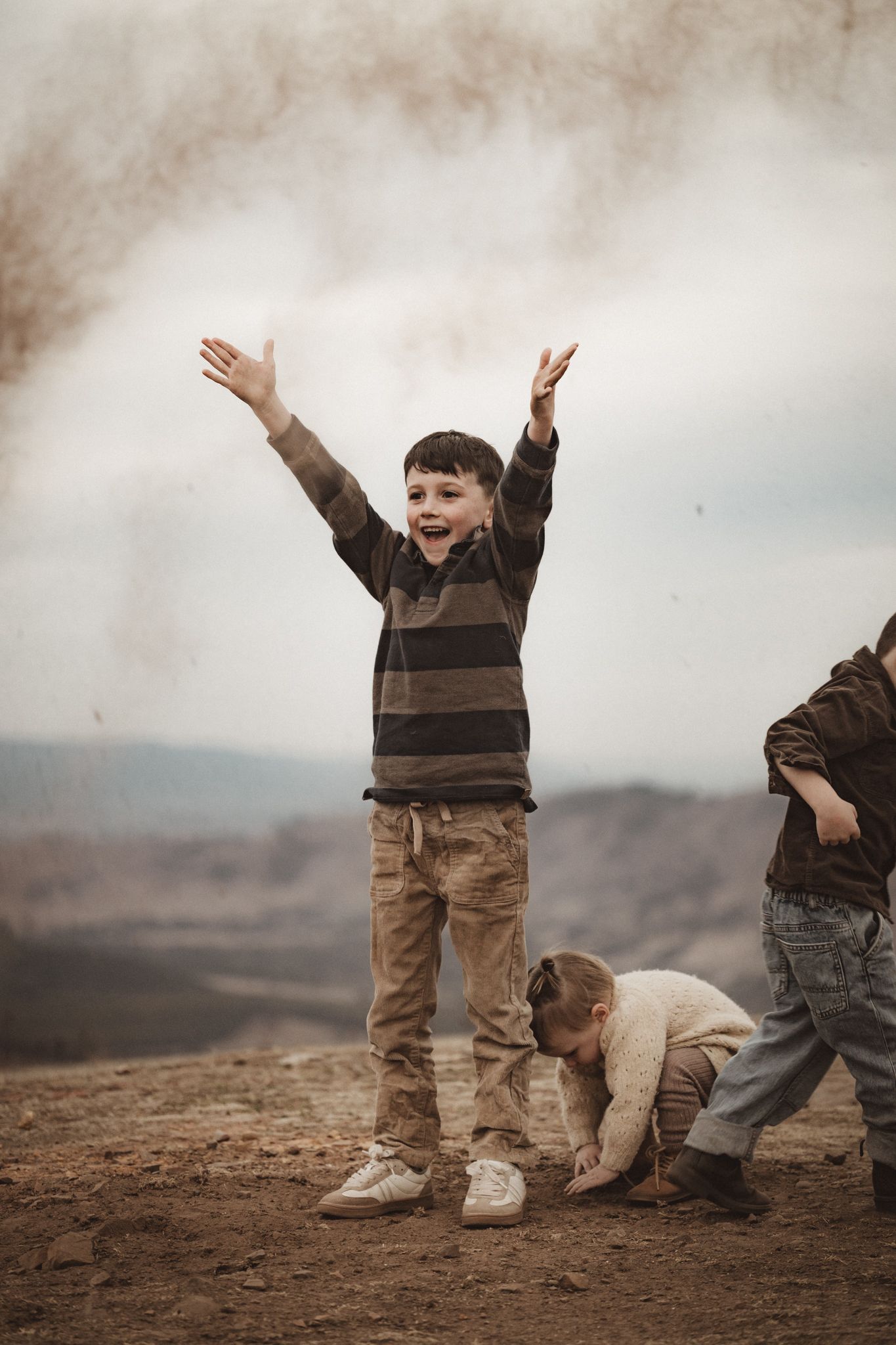 Children playing and celebrating outdoors on a hilltop with moody cloudy skies in the background.