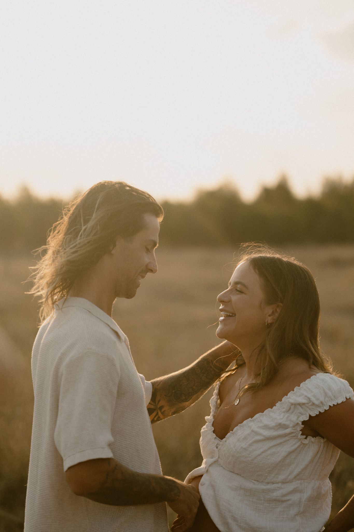 Two people sharing a tender moment at sunset in a field with warm golden light and wind-blown hair.