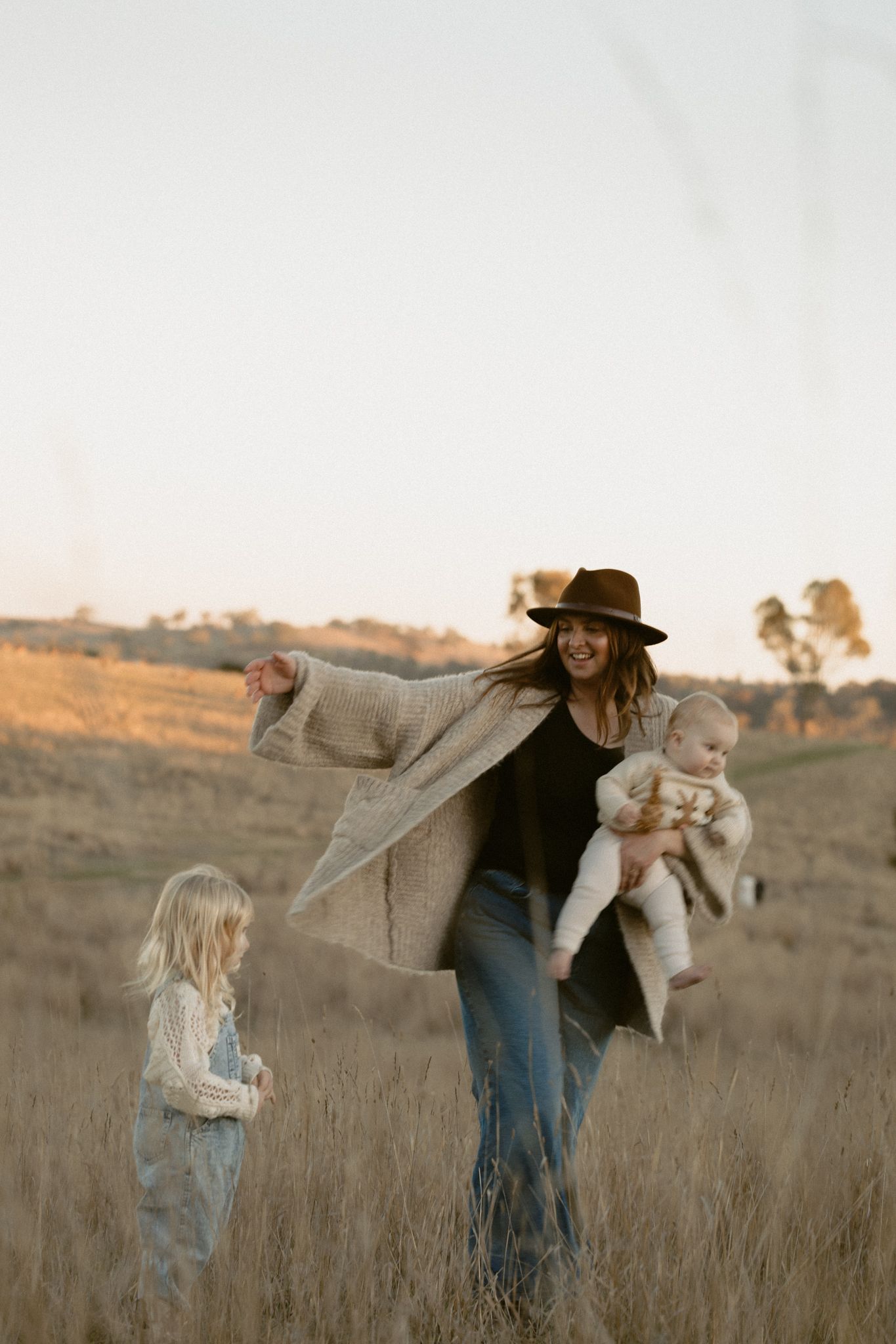 Parent and child share a tender moment while walking through a sun-drenched field at golden hour.