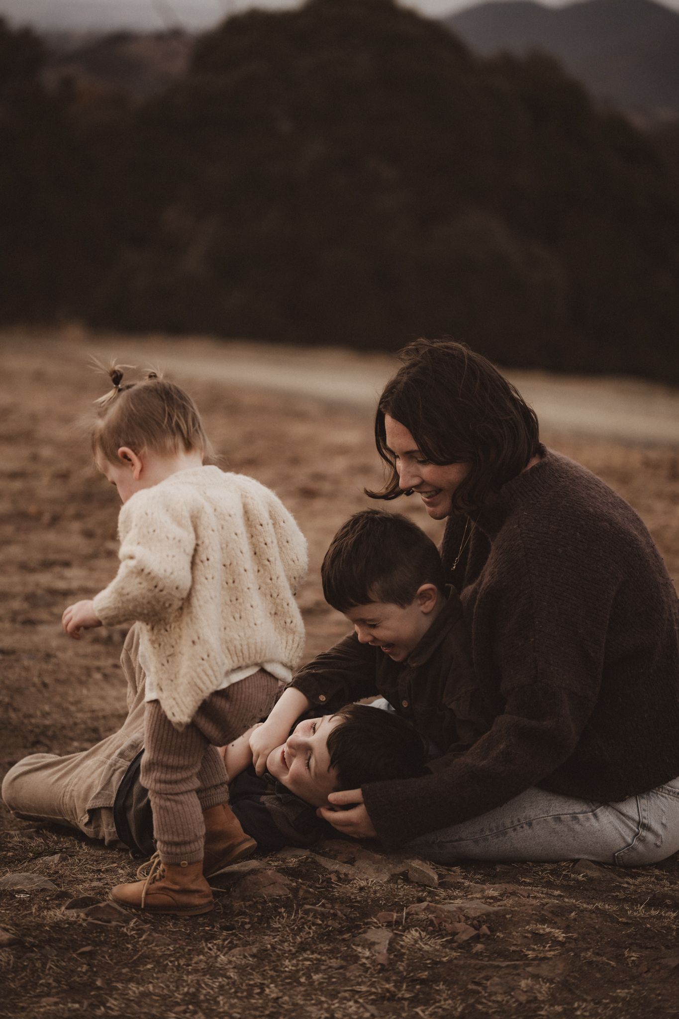 A parent and children sit together on a scenic mountain trail during sunset enjoying quality family time outdoors.