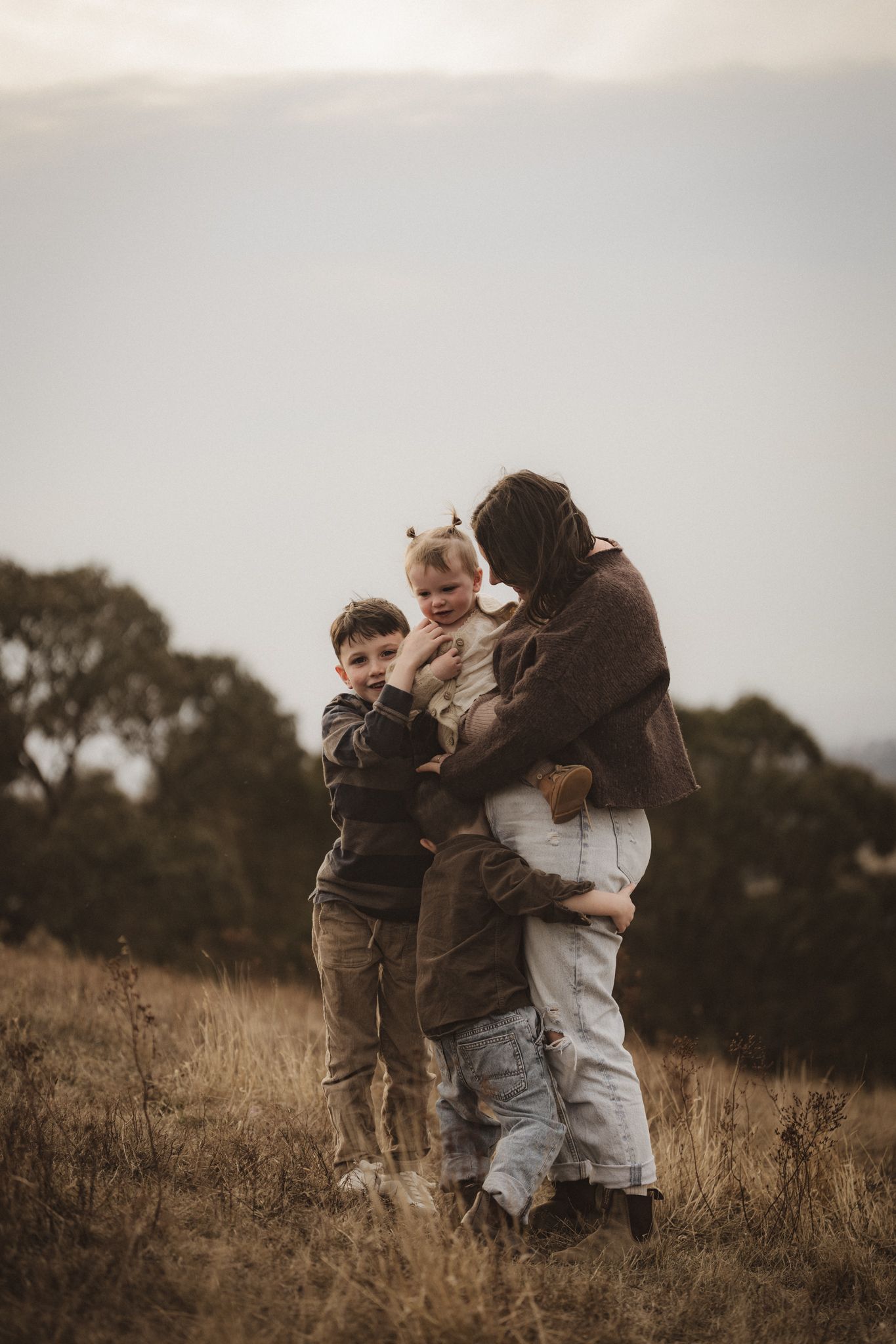 A family shares an intimate moment together while standing in a golden field at dusk.