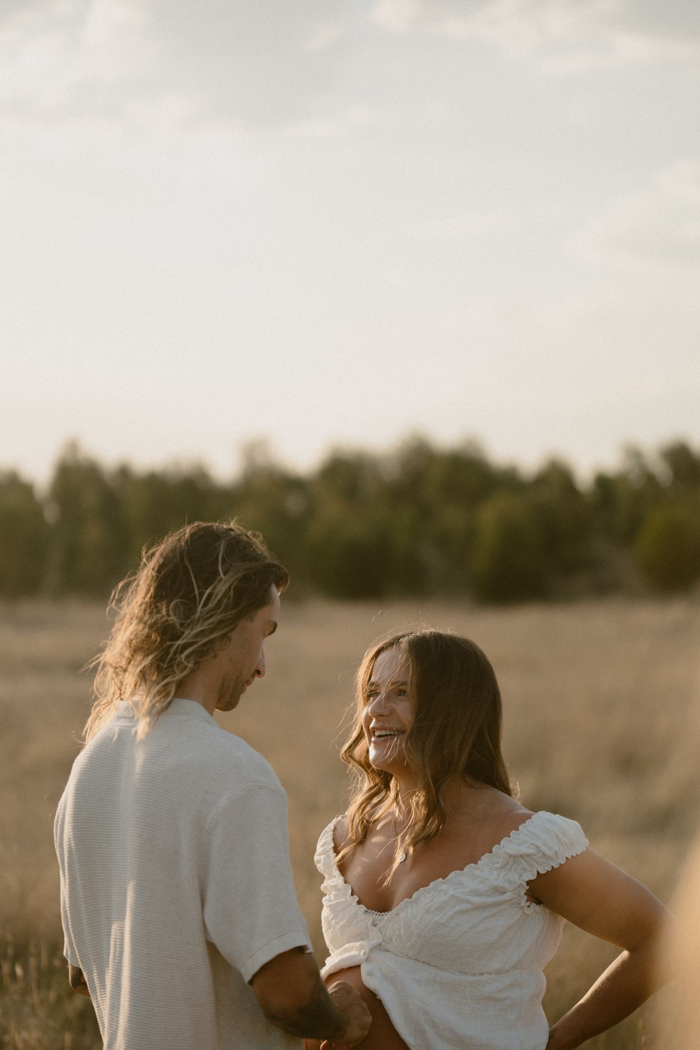 A couple in white clothing sharing a joyful moment together in a sun-drenched field at golden hour.