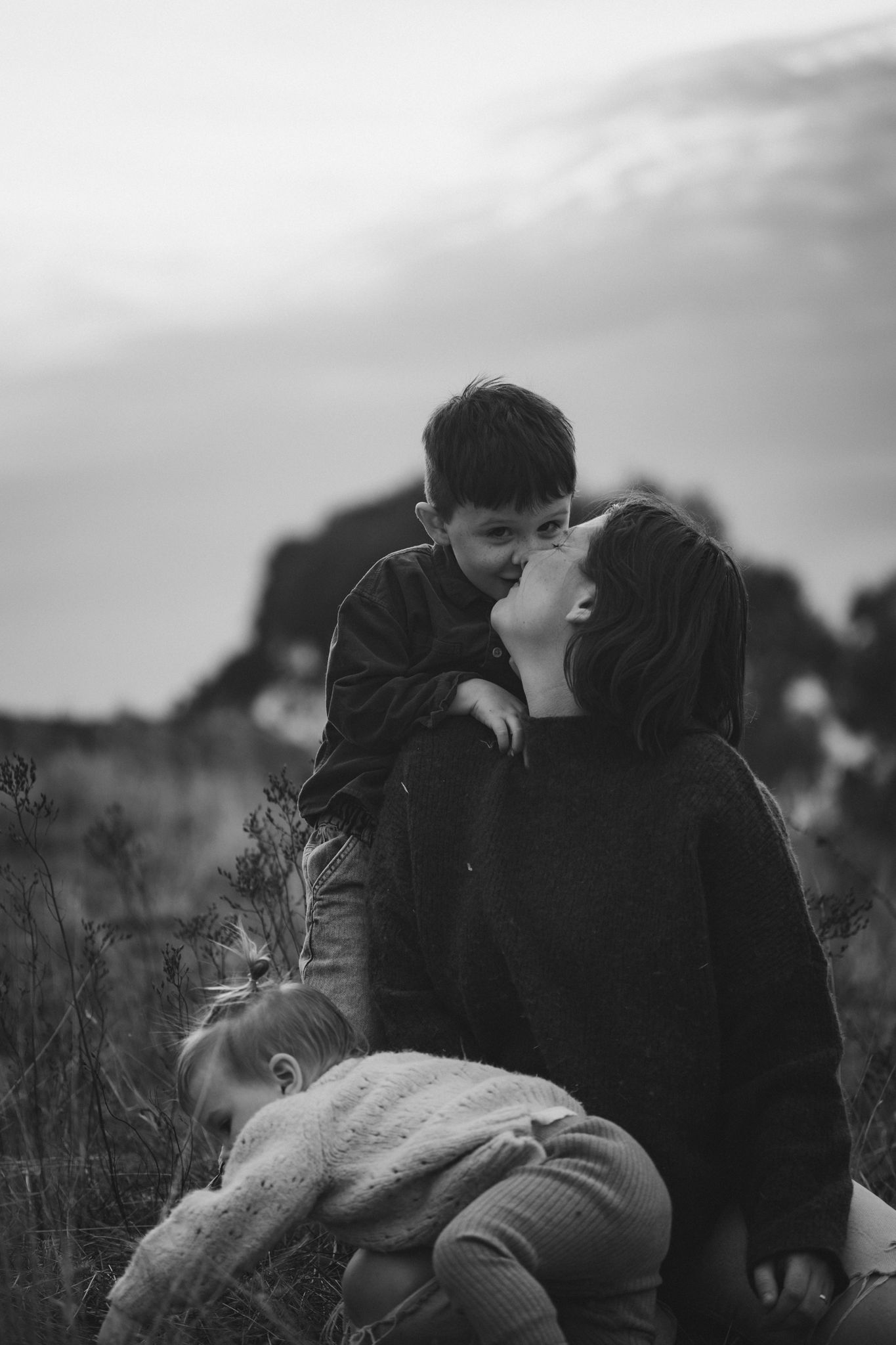 Black and white photo of family members sharing an intimate moment together in a natural outdoor setting.