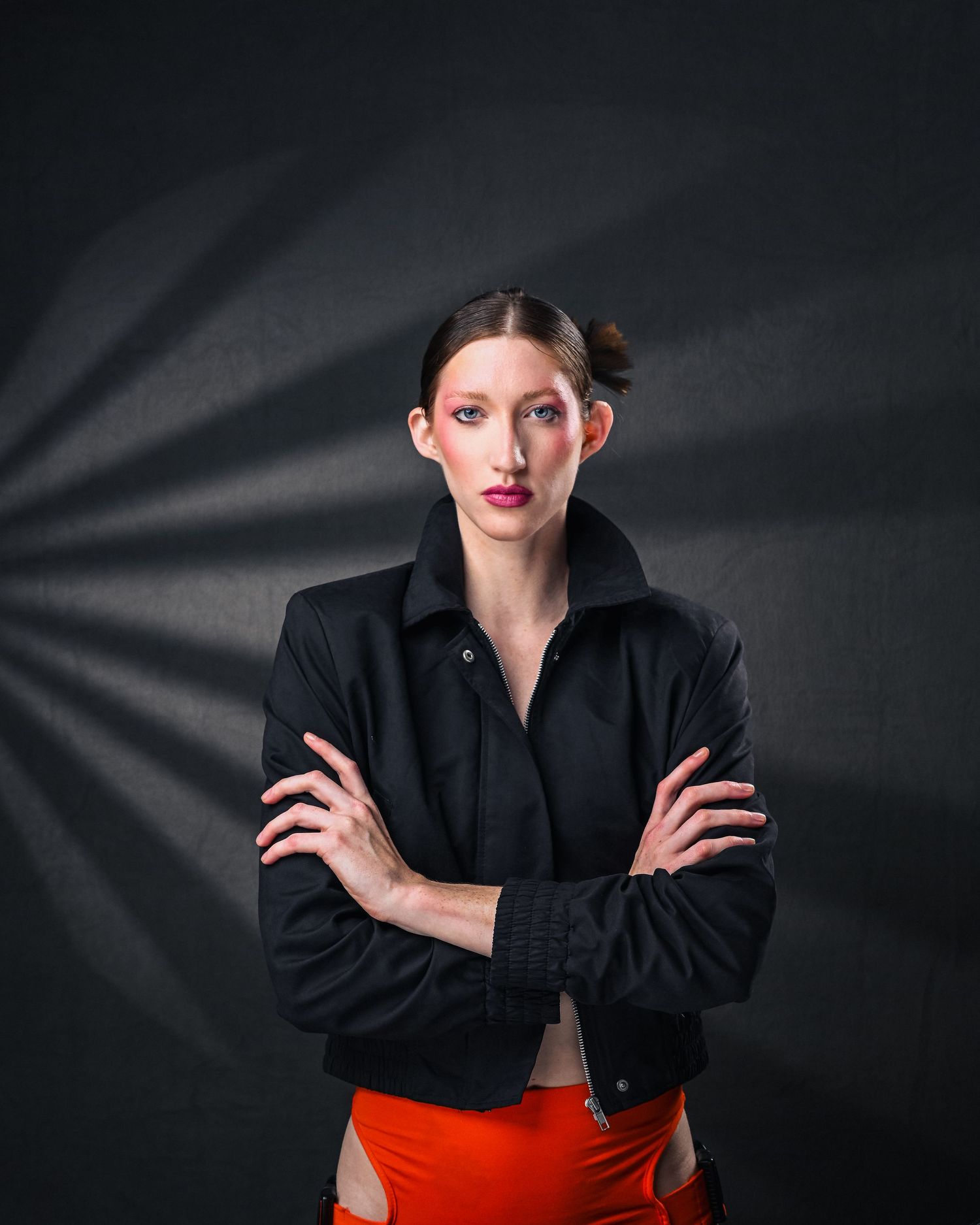 Woman with bold makeup and a black jacket stands confidently against a dark backdrop in a Fort Lauderdale photography studio.