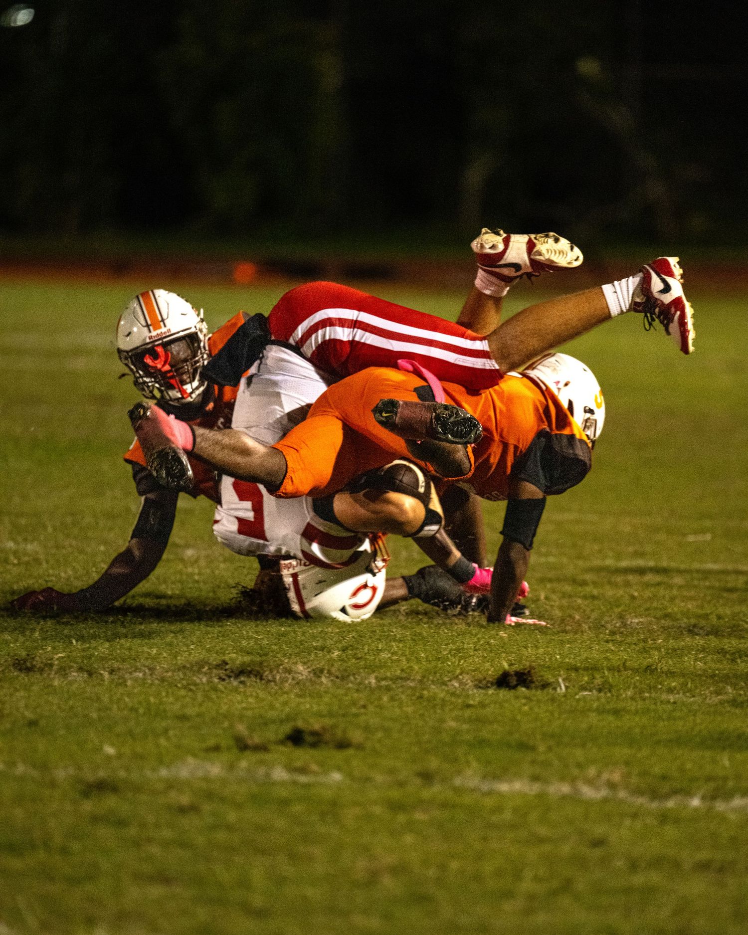 Piper and Plantation High School football players in mid-tackle under stadium lights, capturing intense action. Captured by Ur The Focus