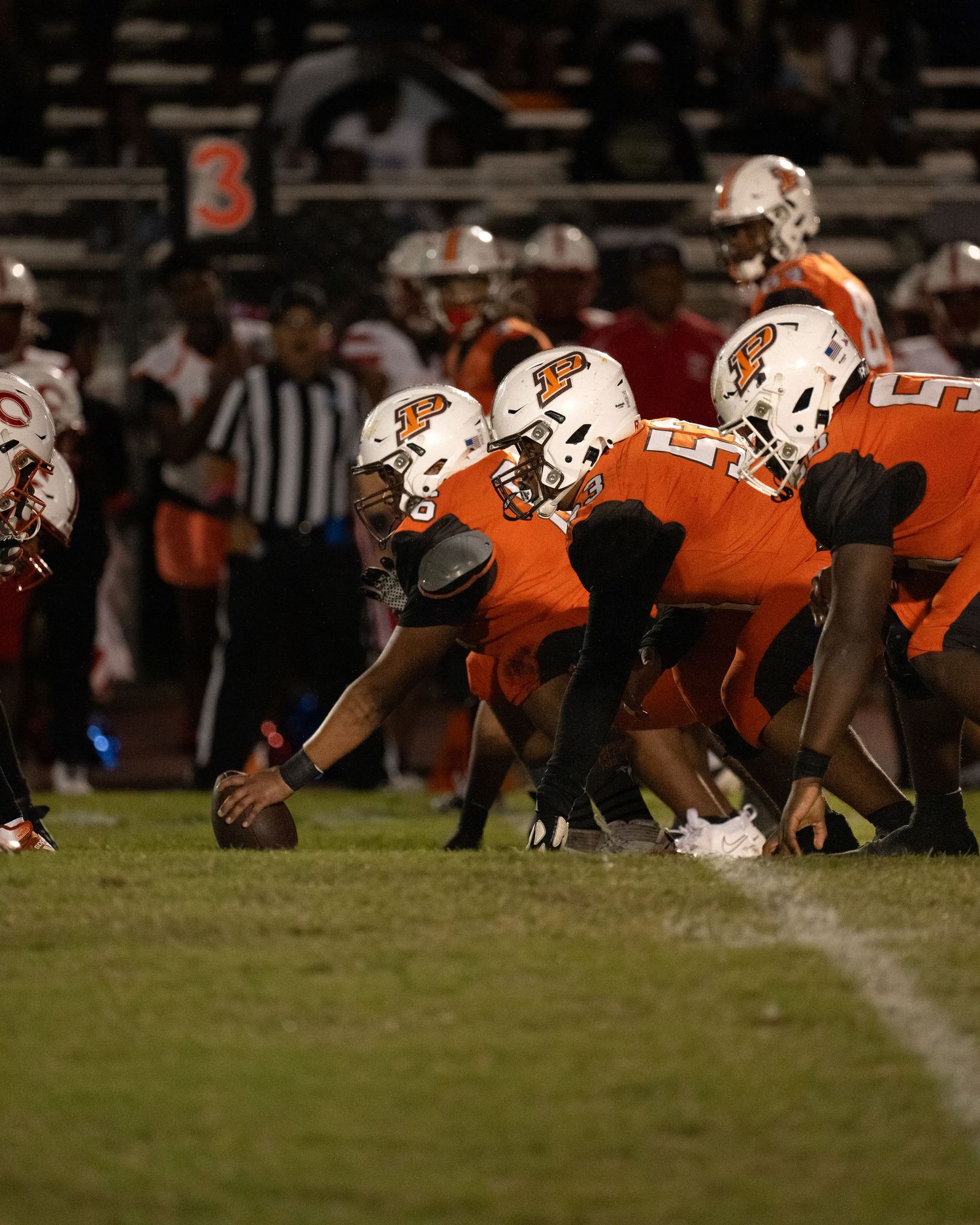 Piper Football team lines up in a pre-snap formation during a nighttime game in South Florida, showcasing strategic gameplay.