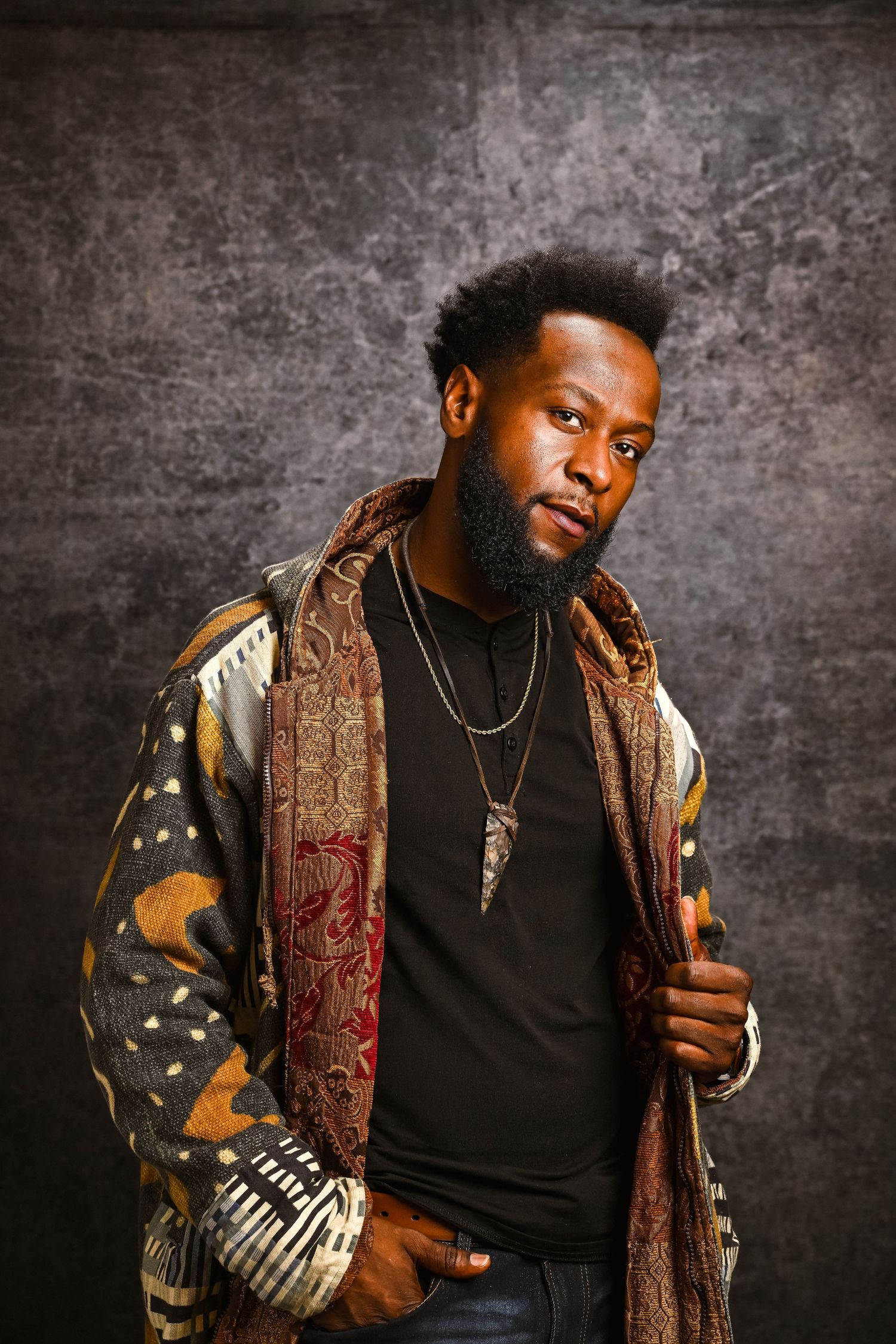Stylish man in layered patterns and earthy tones poses in a studio setting for a creative portrait session with Fort Lauderdale photographer