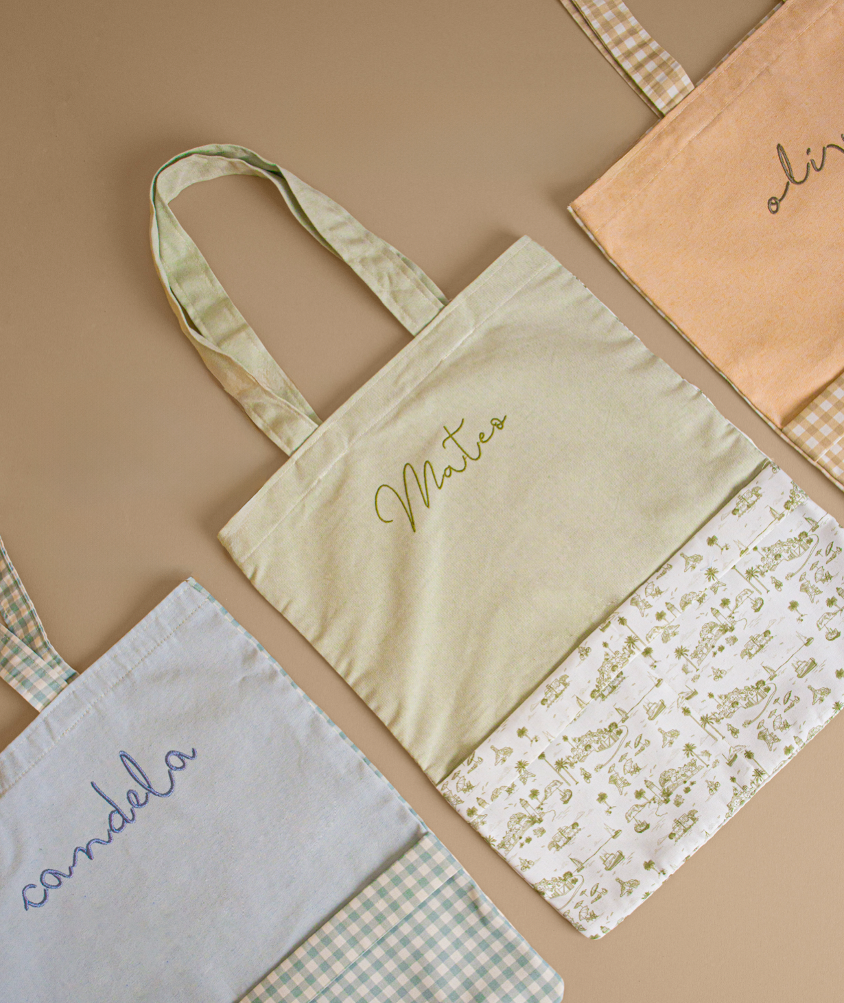 Pastel colored canvas tote bags with embroidered text on gingham and floral fabric backgrounds.