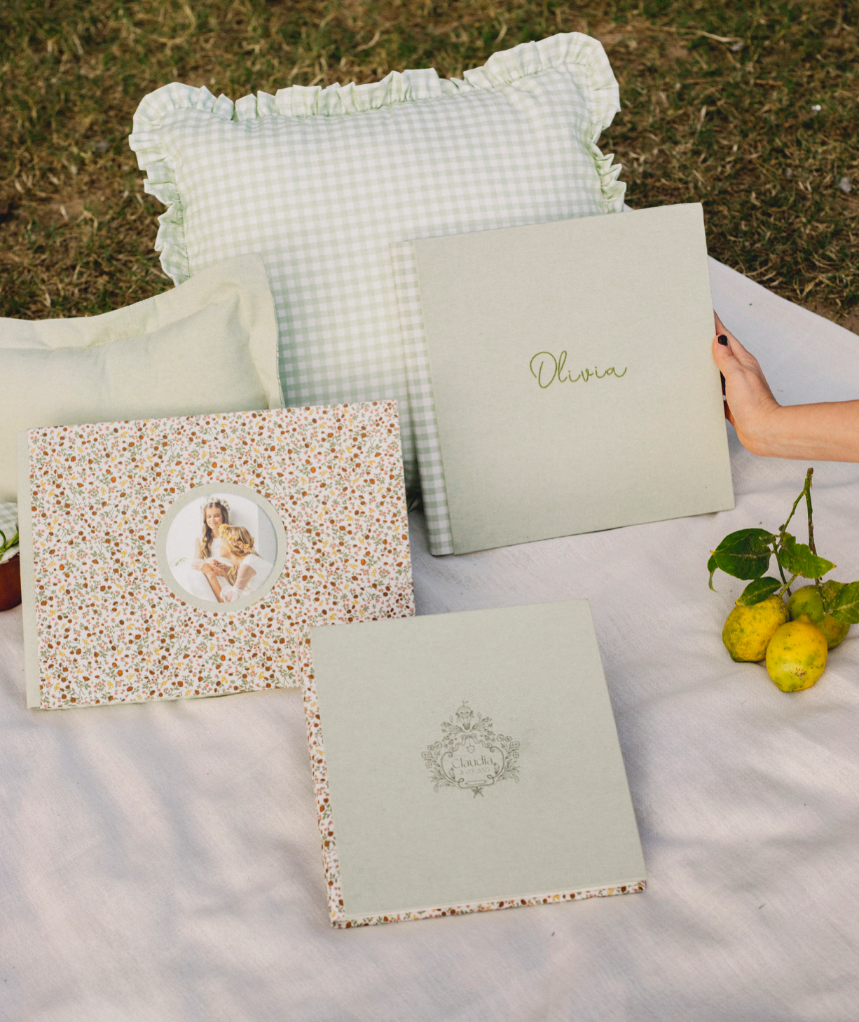 Elegant wedding photo albums and decorative pillows arranged on white linen with fresh lemons in an outdoor setting.