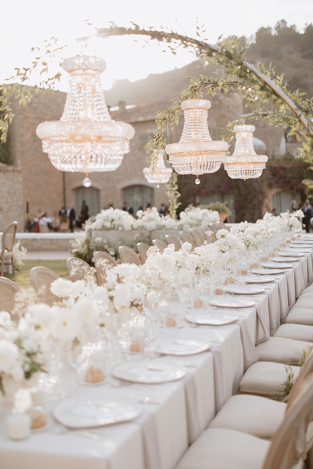 Elegant wedding reception table setting with crystal chandeliers and white floral centerpieces.