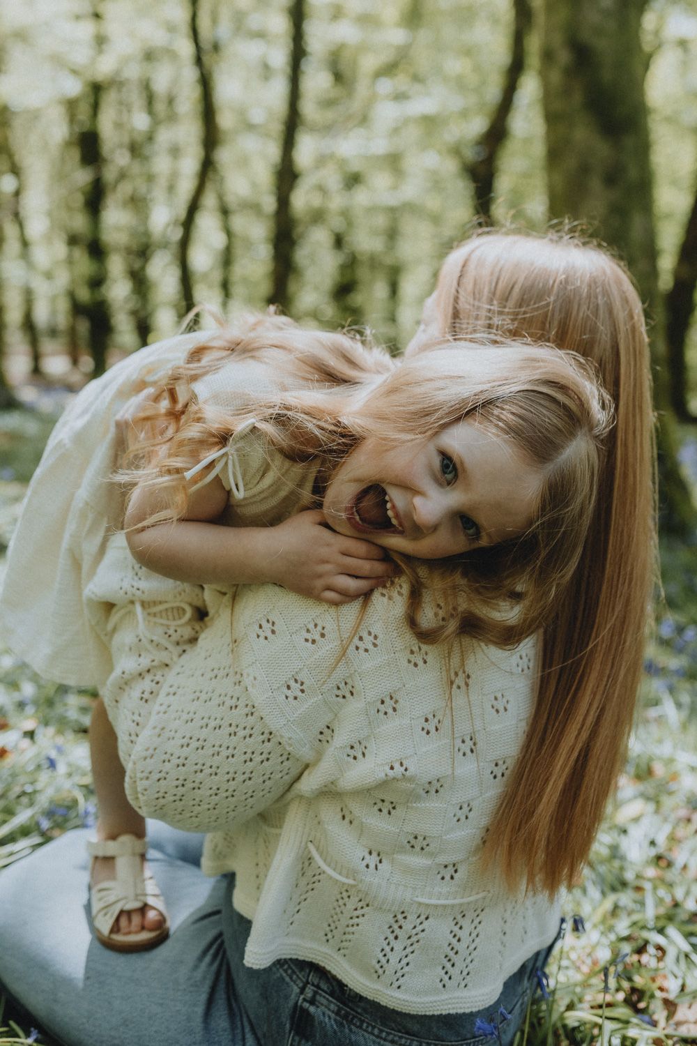 A tender family moment captured in a forest setting with soft lighting and delicate white knit sweaters.