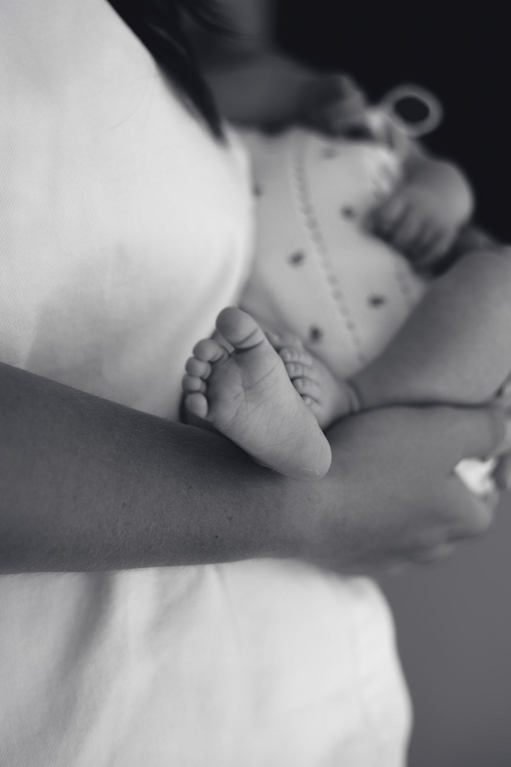 A tiny newborn baby foot rests on white fabric in black and white photography.