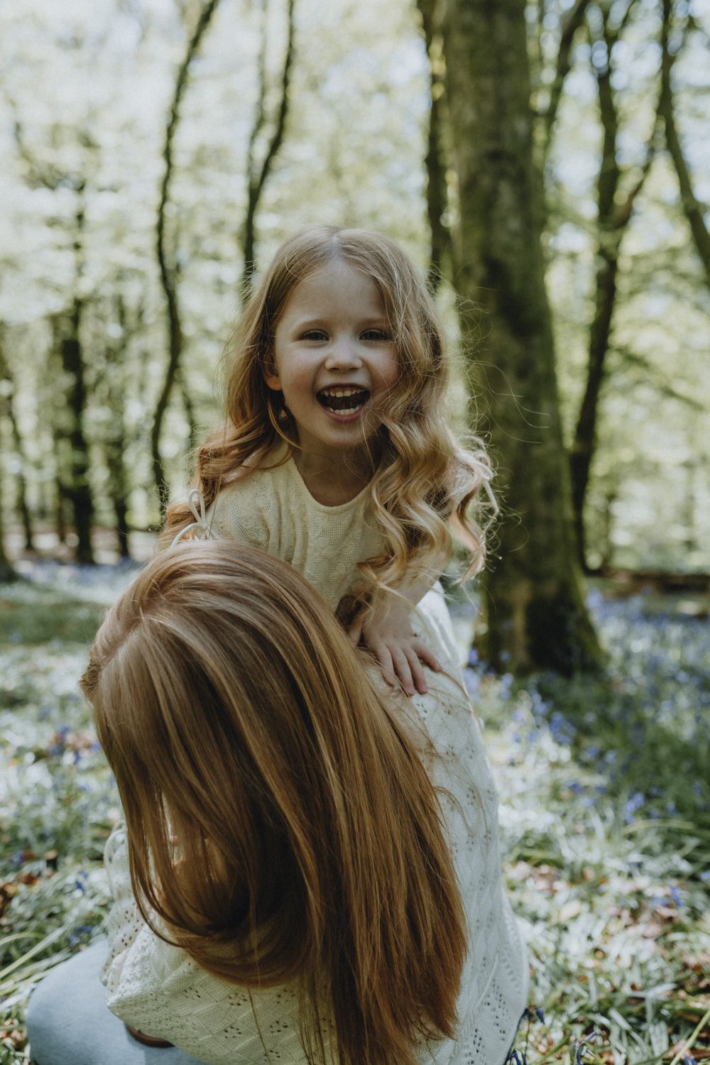 Two smiling children playing together in a spring forest with blooming bluebells surrounding them.
