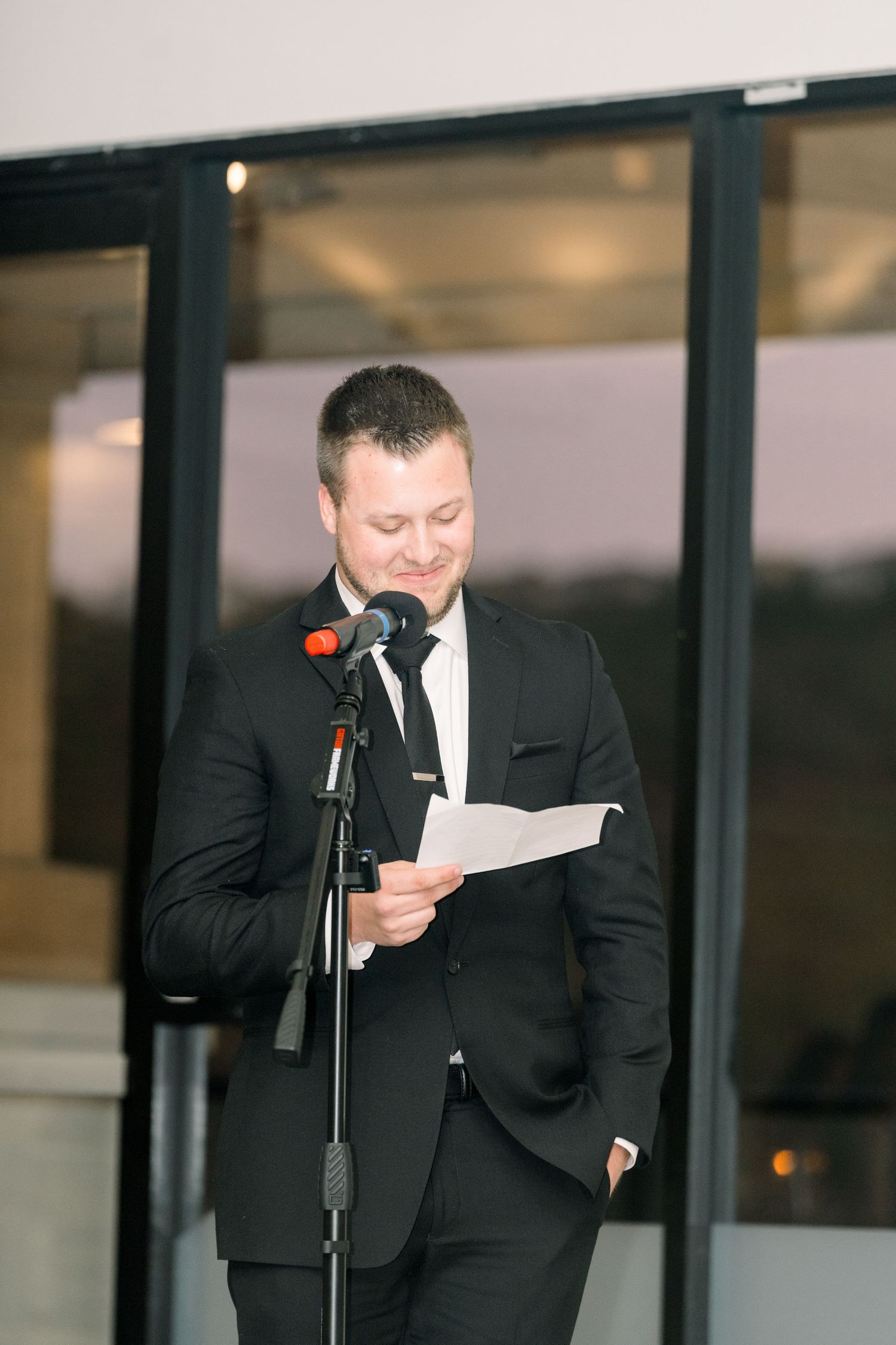 Speaker at formal event reading from paper at microphone podium during evening reception.